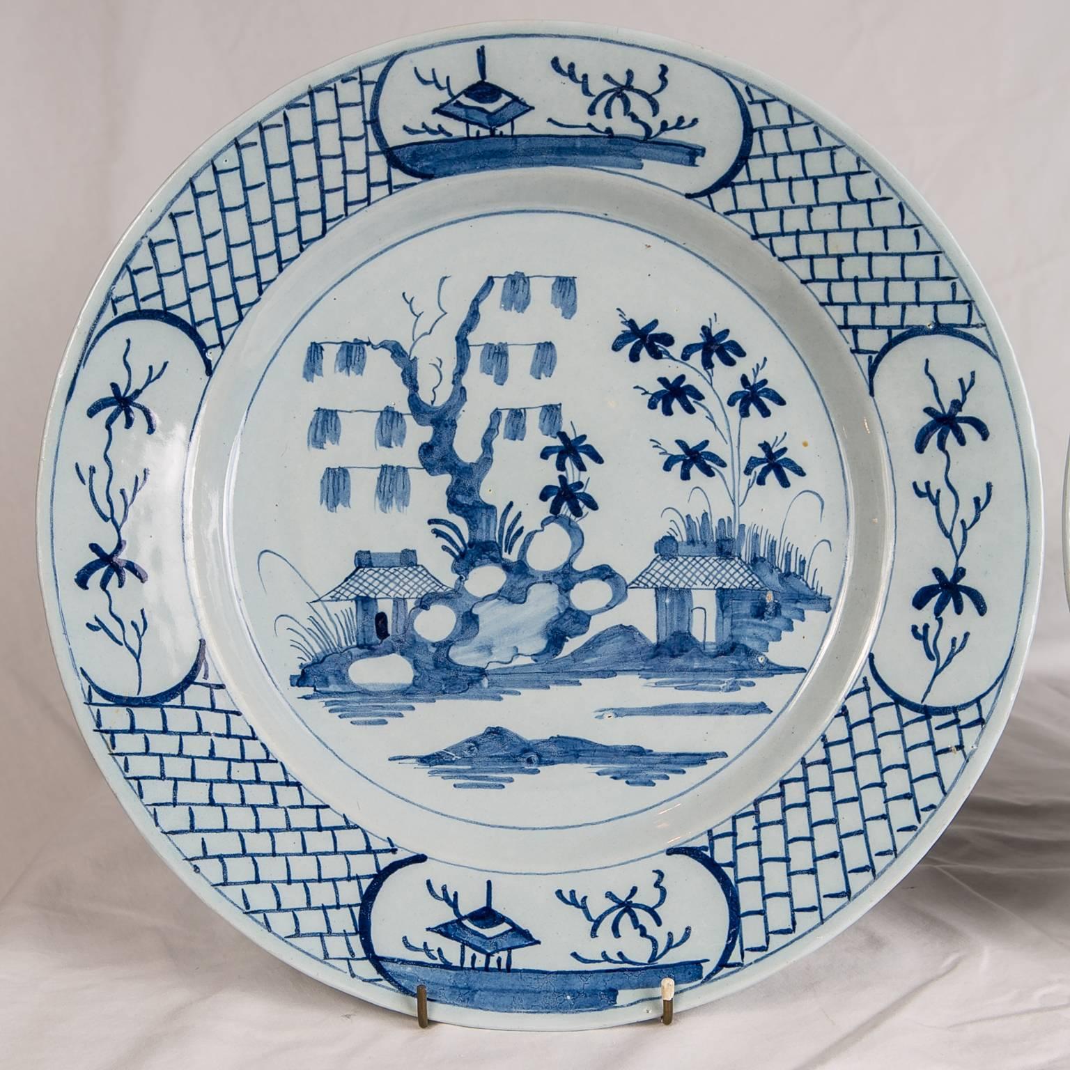 We are pleased to offer this pair of Delft blue and white chargers made in England circa 1760. They are painted in a beautiful soft cobalt blue showing traditional images of chinoiserie decoration: pagodas, flowering trees, and a rocky outcropping.