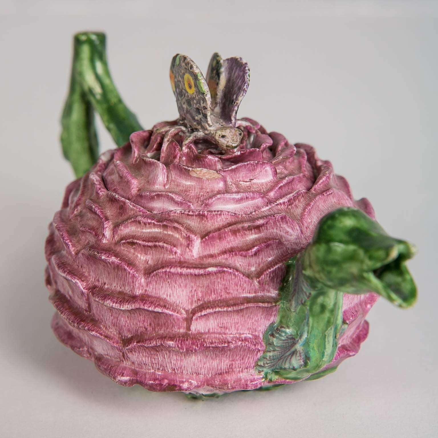 An important Meissen 18th century miniature tea pot in the form of a pink rose. On the cover of the tea pot a butterfly has landed. The tea pot has a green crabstock handle and green spout in the form of a dragon. The bottom is covered with a large