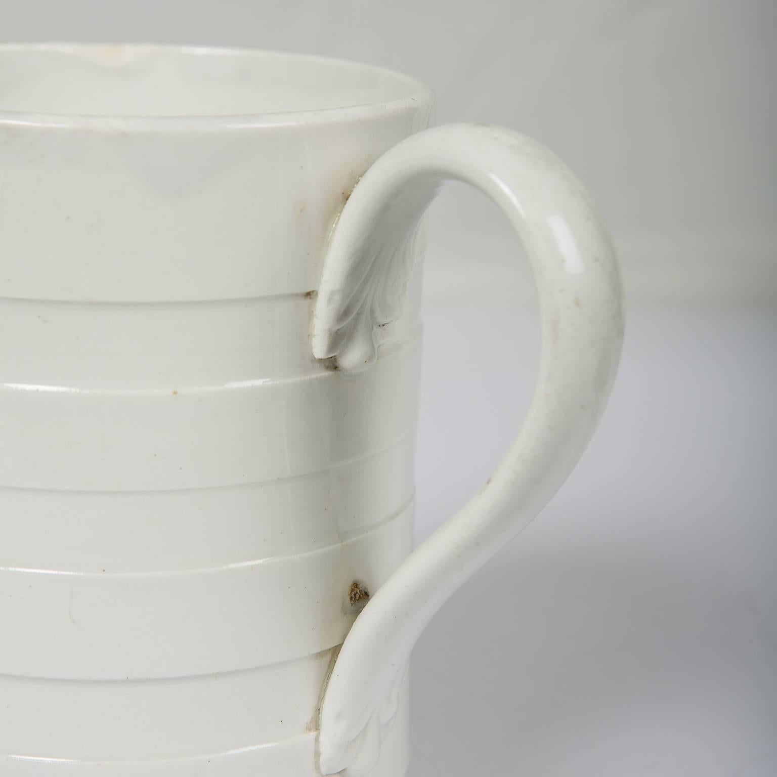 An early 19th century English creamware mug, machine turned on a lathe with indented bands.
The strap handle has traditional foliate terminals. The form is simple and classic in shape.
Today it would look great used either for flowers, or on a desk