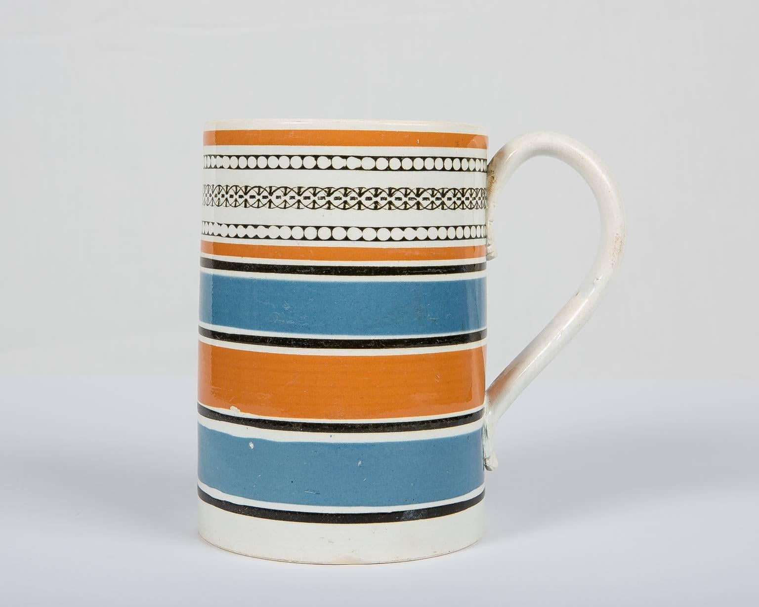 A handsome antique Mochaware quart mug or tankard that is wider at the bottom and slightly tapers as it goes up. Made in England, circa 1820, this mug was decorated with slip in broad machine-turned bands of orange and blue. The top of the tankard