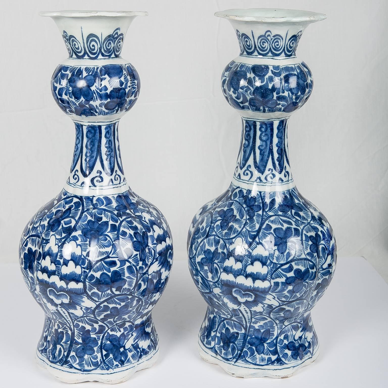 A pair of 18th century blue and white Dutch gourd shaped vases molded with delicate octagonal lobes. Made circa 1780, the Delft vases are hand-painted in deep cobalt blue with a beautiful  design of scrolling vines and flowers. The neck of each vase
