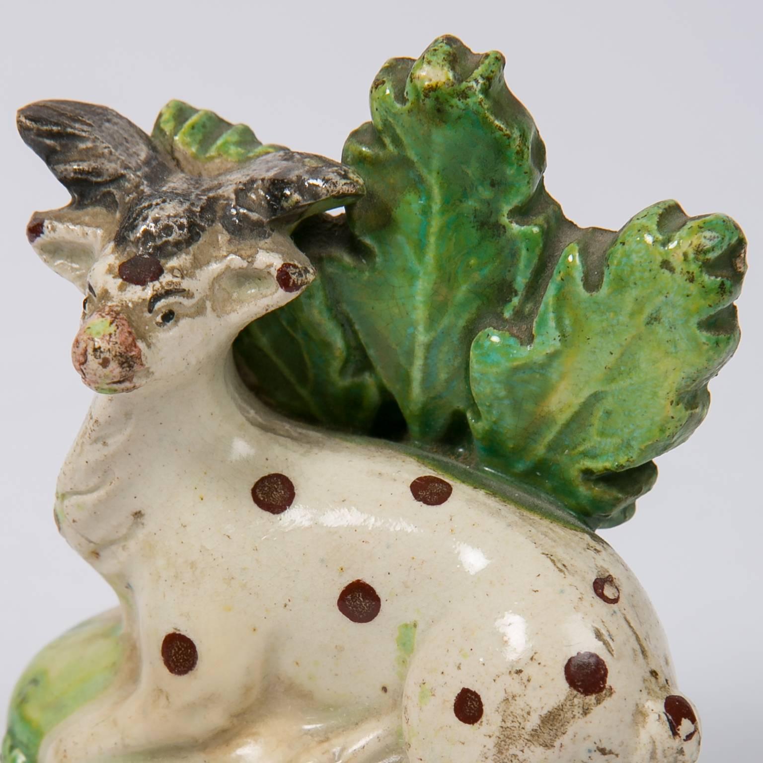 We are pleased to offer this 18th century Staffordshire creamware figure of a spotted white tailed deer modeled resting on a green grassy base with a bocage of three large leaves. The figure is open on the bottom the way early Staffordshire figures