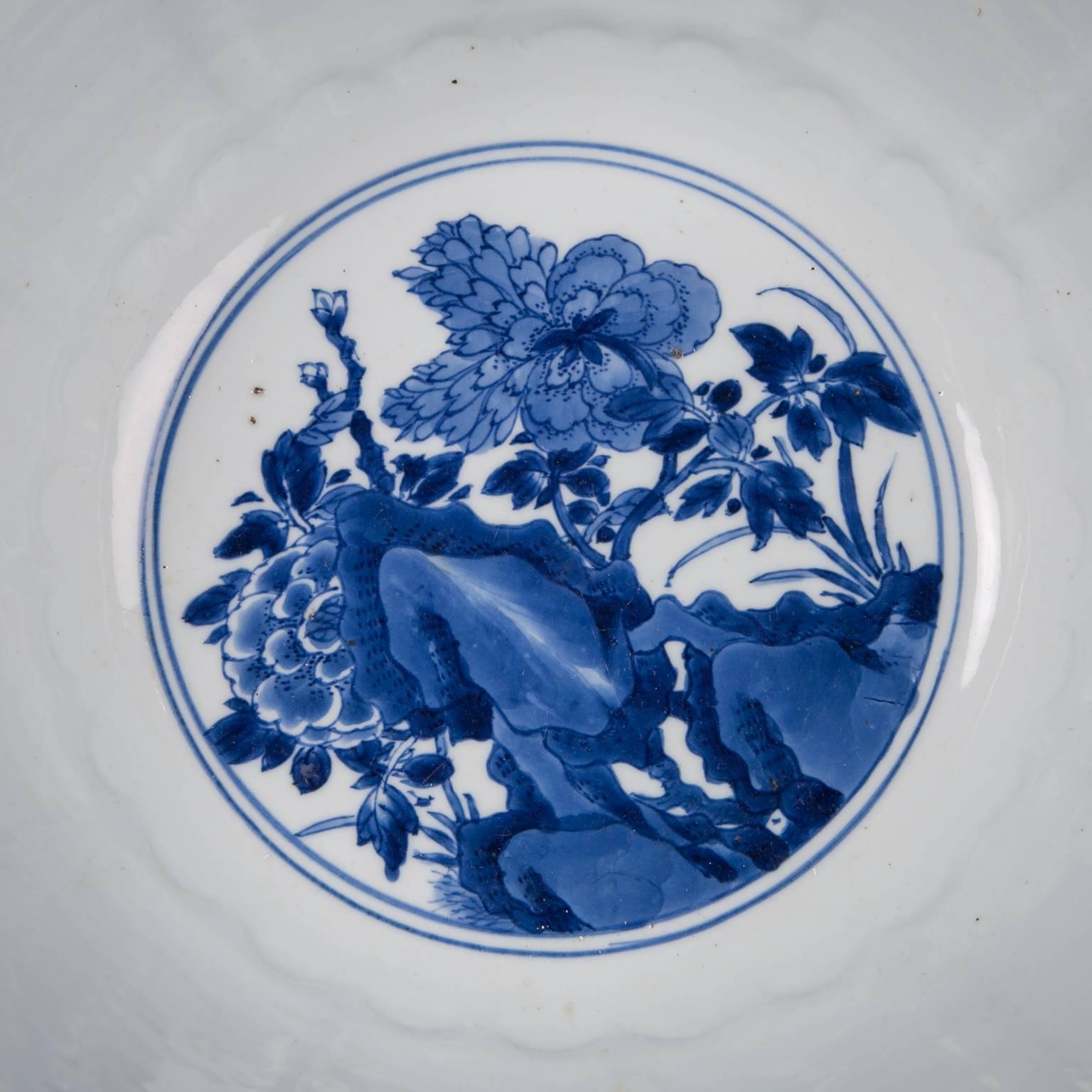 A pair of Antique Chinese Kangxi blue and white bowls. These large punch bowls are decorated to the outside with a variety of auspicious flowers framed in lotus petal panels. Flowers such as hydrangea, plum blossom, peonies, peach blossom all