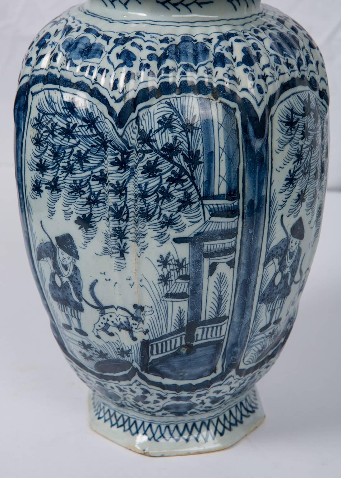 A lovely blue and white Dutch delft jar with panels painted in deep cobalt blue.
The vase shows a chinoiserie scene of a boy and his dog walking near a pagoda style pavilion with a tree on a fenced terrace.
The covered jar is topped by a traditional