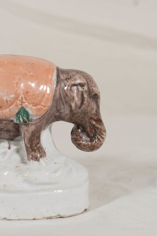 A pair of fanciful Staffordshire figures of elephants each with an orange saddle blanket modeled standing on an oval base.