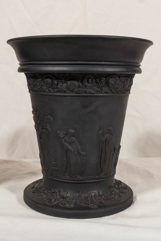 A pair of Wedgwood black basalt vases with molded decoration in relief,
showing scenes with classical figures between bands of flowers and fruits. 
Black basalt was created by Josiah Wedgwood in the 18th century. Wedgwood transformed Egyptian