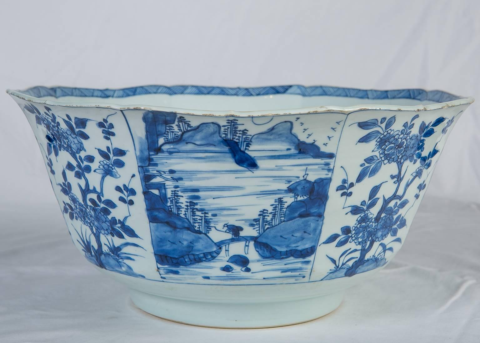 Kangxi Chinese blue and white porcelain punch bowl, circa 1700. Painted in underglaze cobalt blue, the bowl is decorated to the exterior with alternating panels showing flowering fruit trees and scenes of mountains, along the seashore. The bowl has