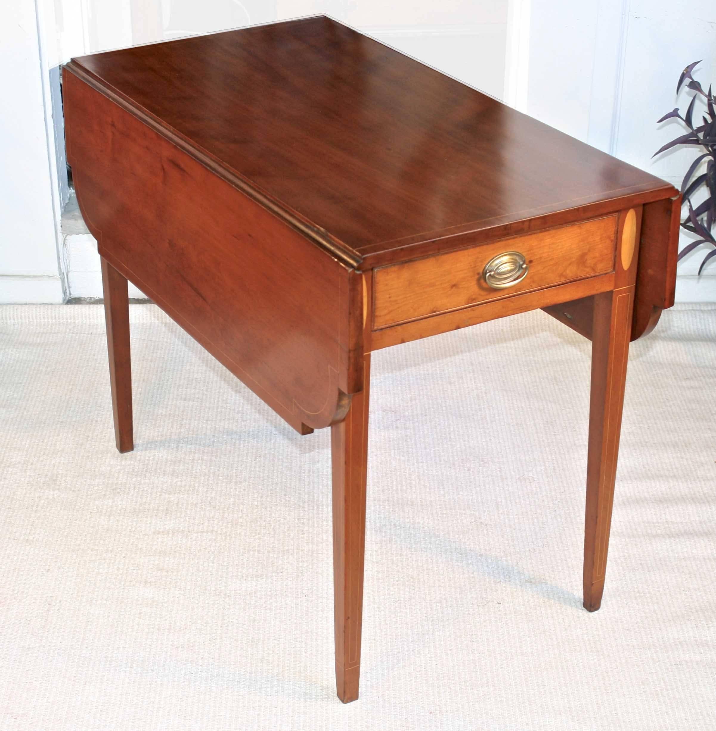 In the Hepplewhite manner, a satinwood fine line-inlaid cherrywood drop-leaf Pembroke table with quarter-round inset corners. Both its functional and faux bead-edged drawer fronts are surrounded by elliptical satinwood inlays. Its brass bale pulls