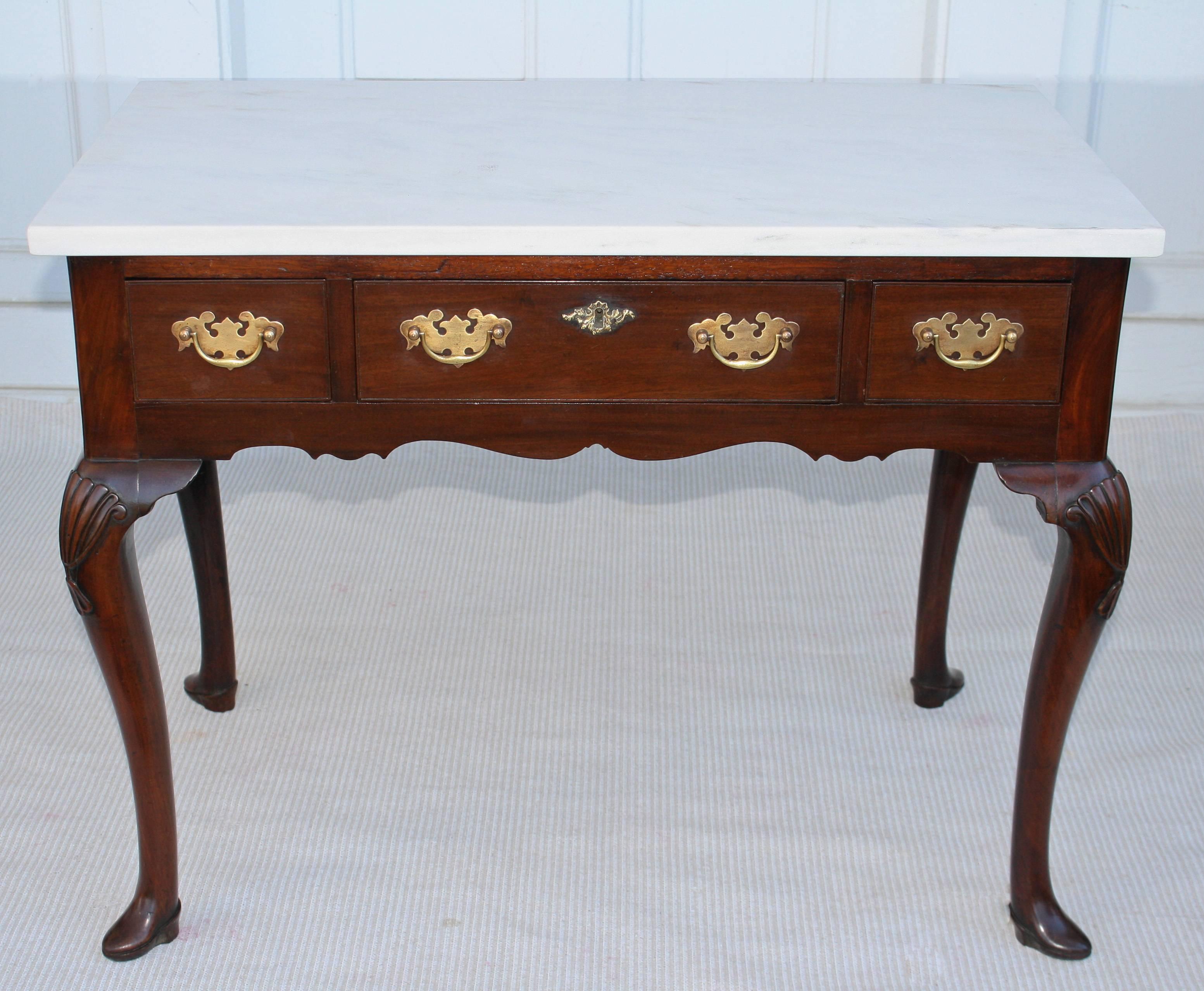 A rare and unusual boot-footed mahogany three-drawered lowboy mixing table, with a white faintly grained Carrara marble top and shell carved knees. The mahogany appears to be Bahamian.  The four cabriole legs with booted or slippered feet, more