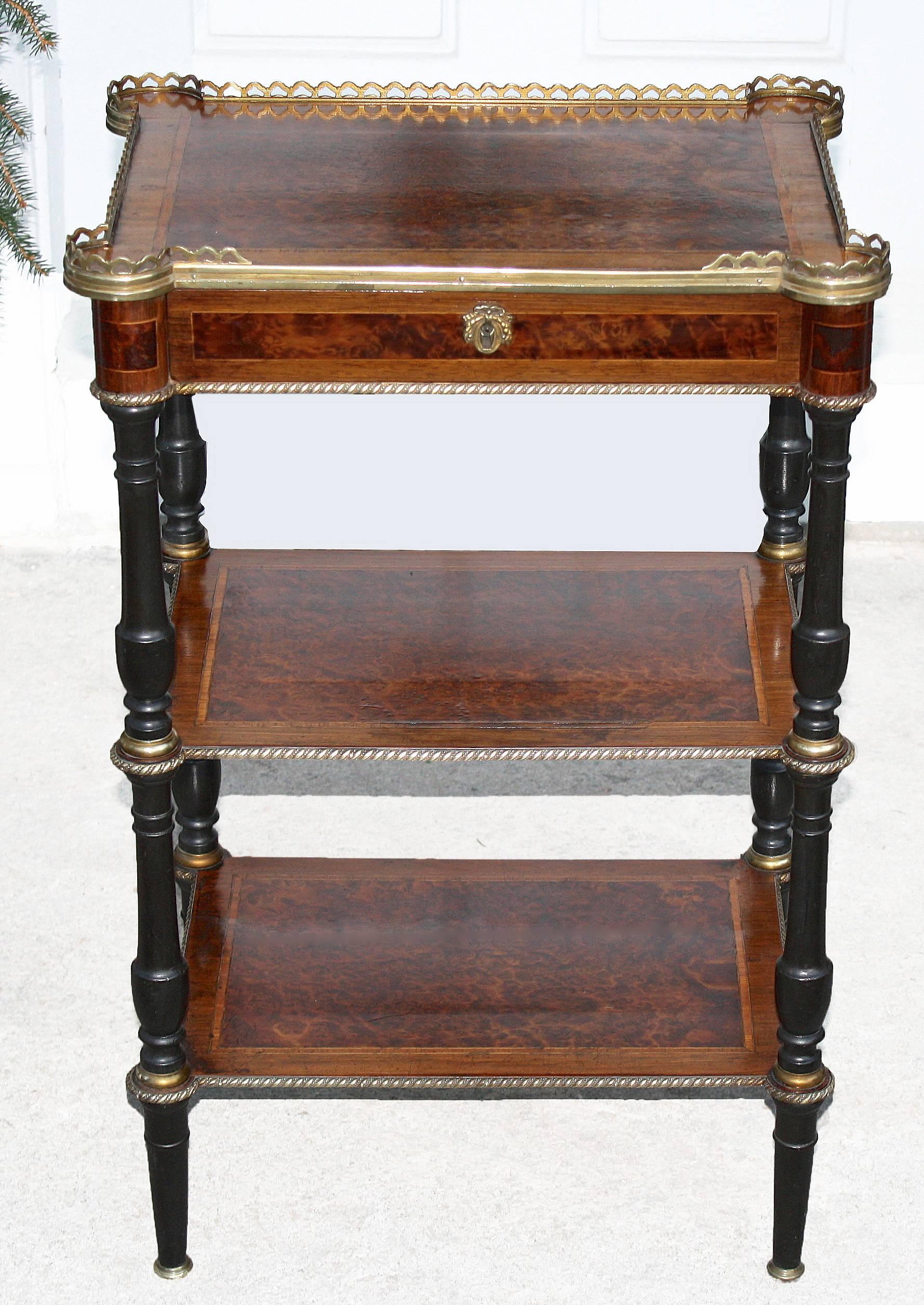 Ormolu galleried and trimmed triple-tiered turret-cornered table with turned ebonized legs. Complex specimen veneers, bandings and inlays of burl, rosewood and satinwood. Drawer with original lock. Remains of a P. Sormani paper label on dust board