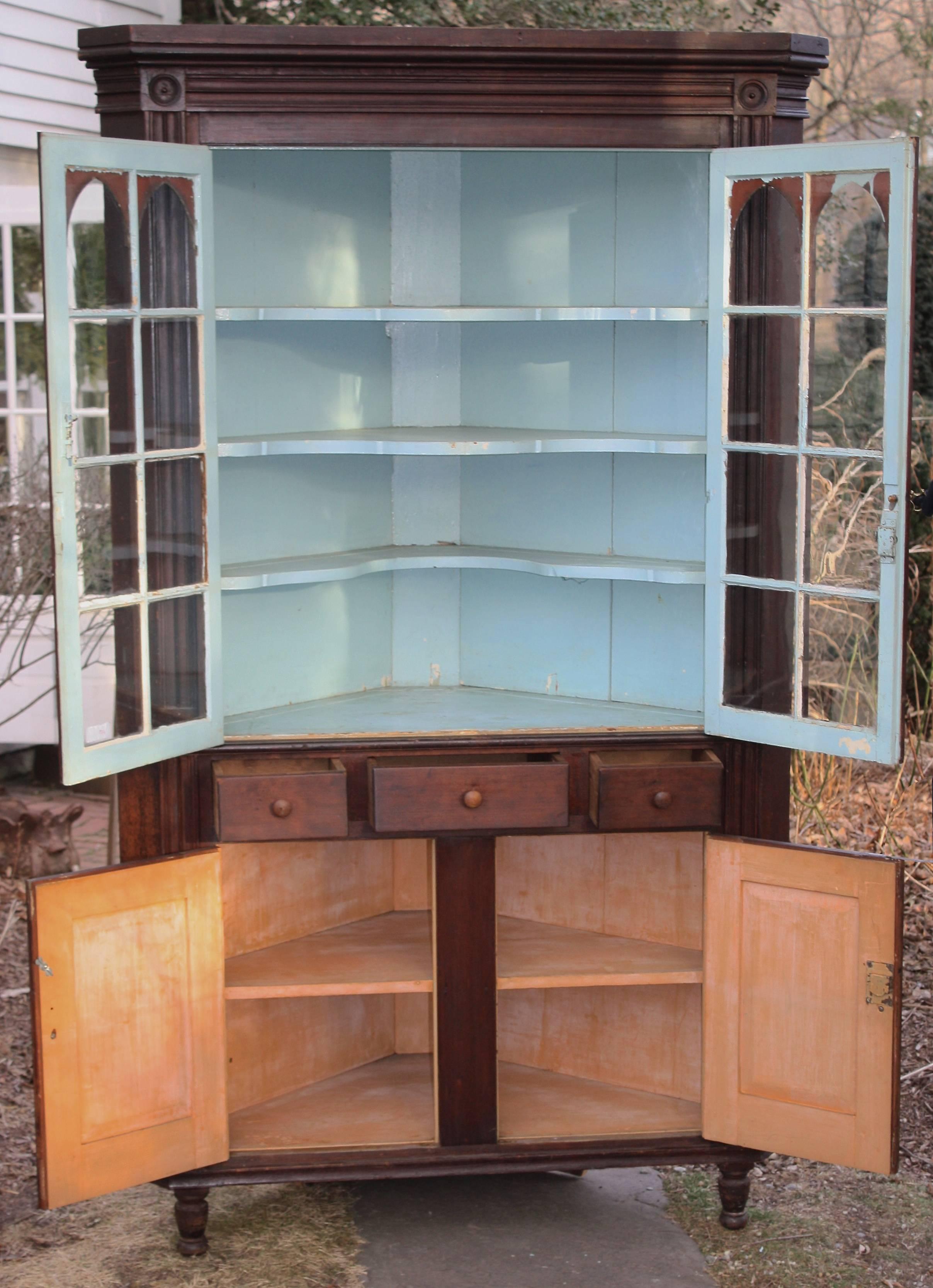 An imposing two-part 'mahoganized' cherrywood corner cabinet in the Sheraton manner; in original finish with mostly original glazing. Gothic applied mullion arches, stubby turned feet and cherry primary wood; likely Middle Atlantic states origin,
