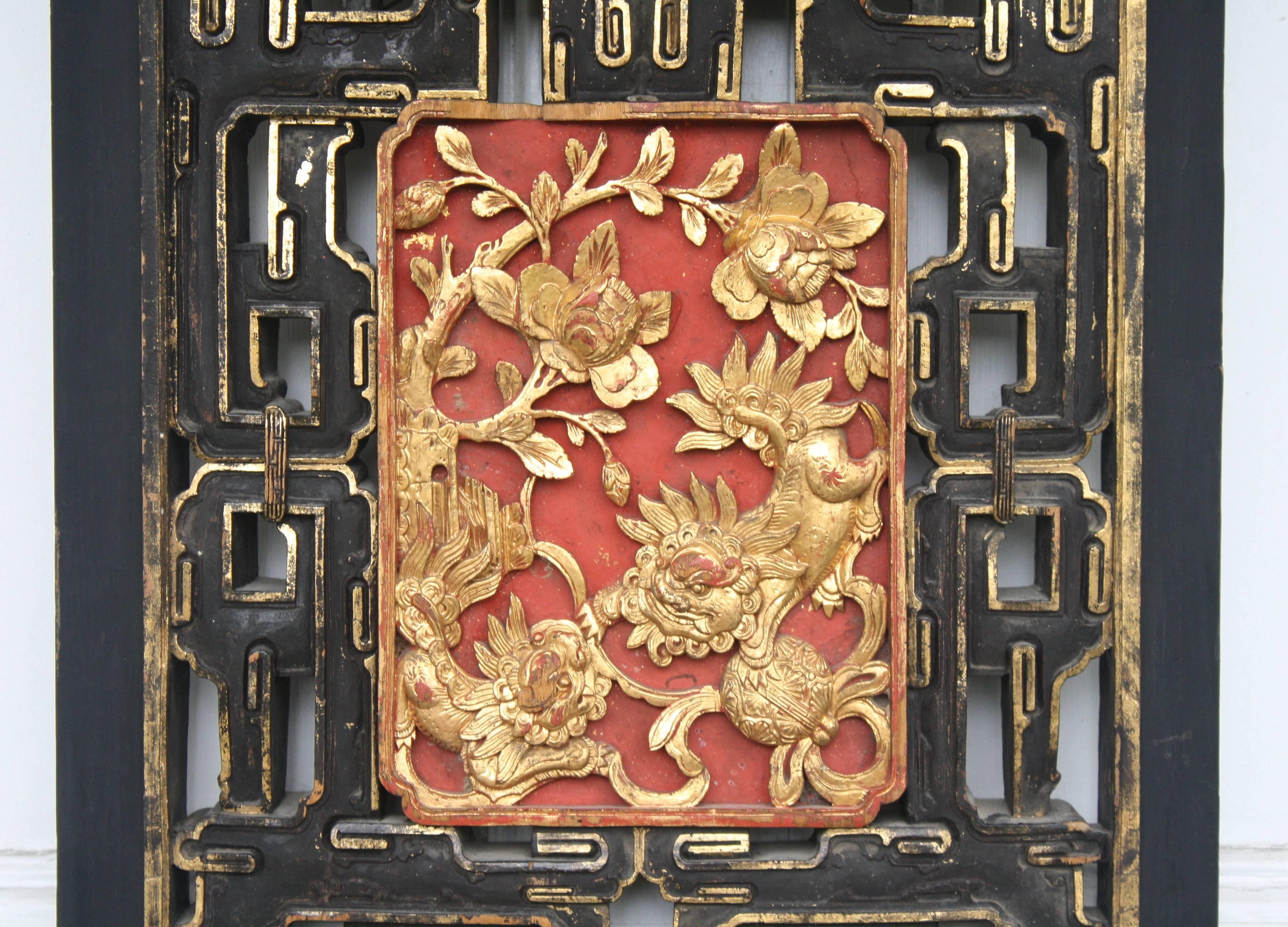 A pierce-carved door panel 'inset' of the Daoguang reign, featuring a center plaque of two gilded sentry lions among foliage on a solid red background. The surrounding pierce-carved framing is ebonised with applied parcel-gilt. The reverse side of