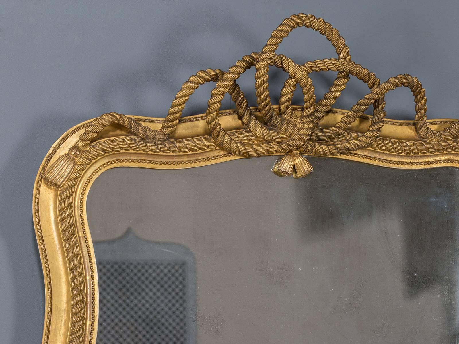 The intricate giltwood knot bow that adorns the top of this mirror is fully three dimensional and gives this antique English mirror its charming appearance. The gently curved sides of the mirror showcase the flow of the rope used to create the knot