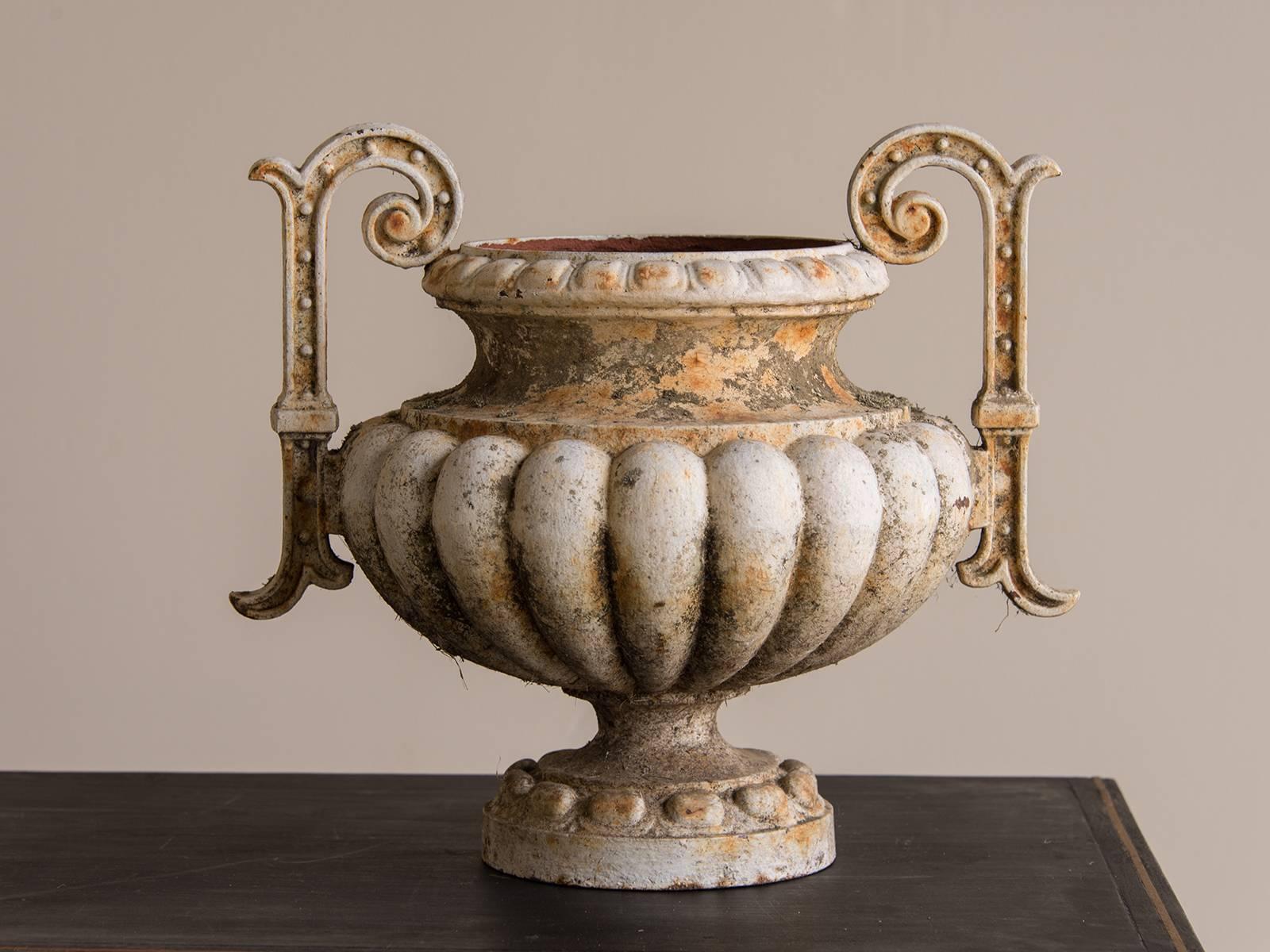 This pair of antique French iron garden urns are modeled after the famous example from the Alfred Corneau Foundry in Charleville, France. The distinctive lobed body is set upon a slender neck and circular base and features a pair of tall handles