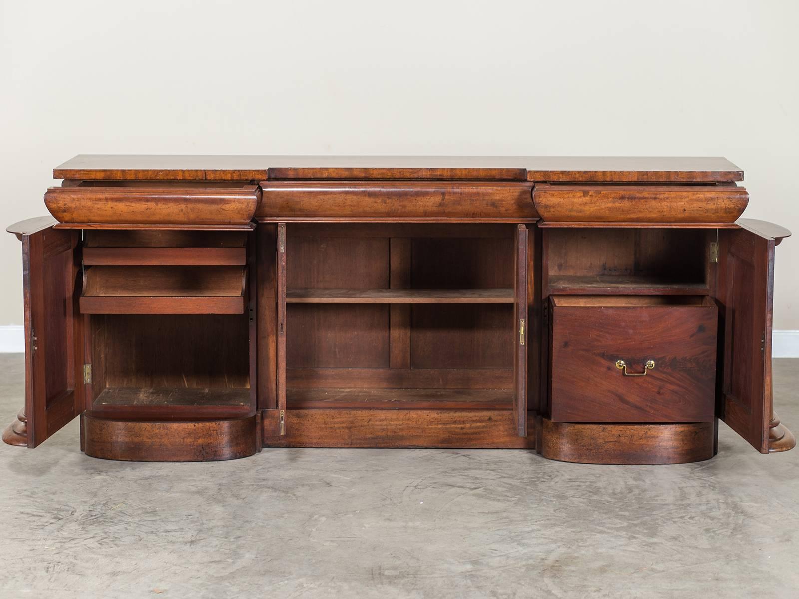 The powerful architectural profile of this antique English Regency sideboard buffet, circa 1825 showcases the exceptional grain of the mahogany timber used in its construction. The left and right cabinet door each feature a tapered column pilaster