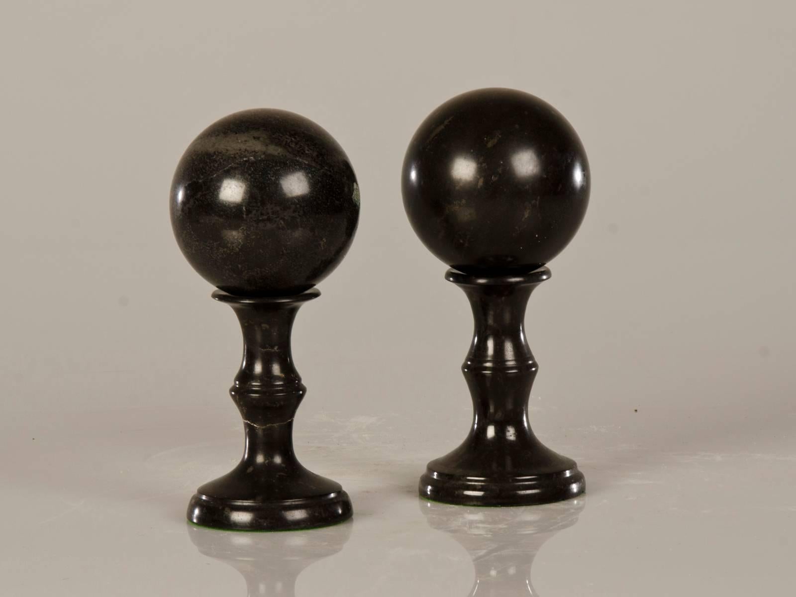 A pair of beautiful antique Italian black marble spheres placed upon baluster shaped column stands from Italy, circa 1890. Each sphere is fully removable from its stand to be able to be held within the slightly cupped top of each stand or placed