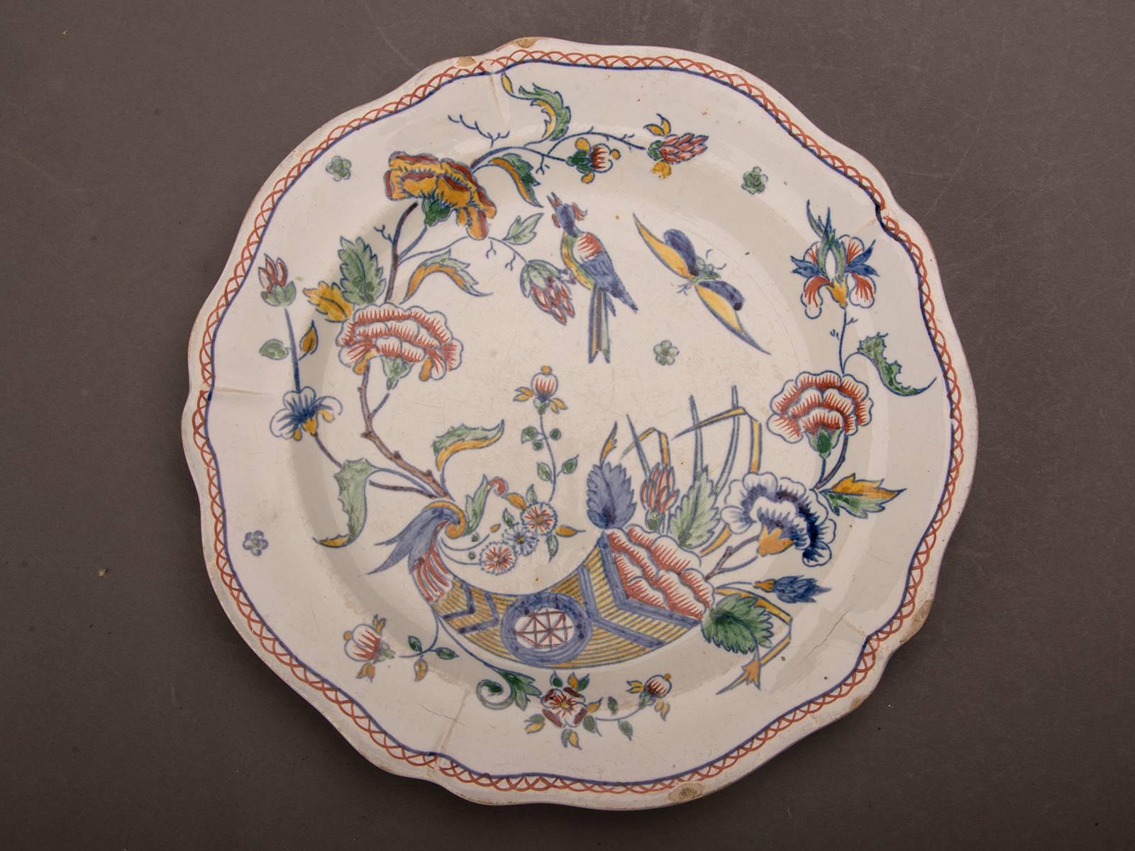 Three individual antique French Gien plates, circa 1860 with hand-painted multi-coloured floral, bird and Horn decoration and a scallop edge shape. The distinctive faience finish with its low lustre glaze is immediately apparent as it imparts a