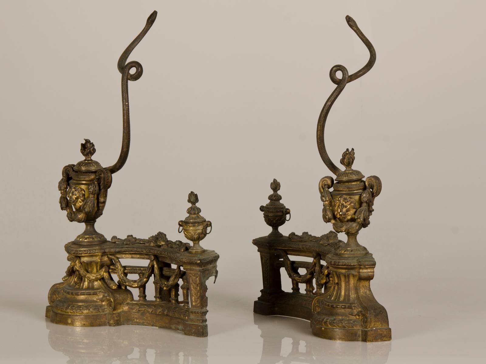 A pair of antique French Louis XVI style aged bronze doré chenets (in English firedog or andiron) from Belle Époque period France circa 1890 featuring entwined serpents set within an architectural base. These unique fire place accessories are a