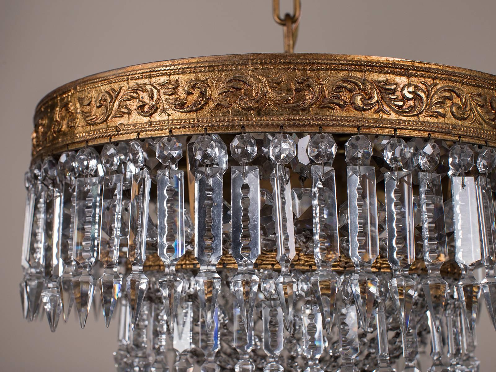 The elegant placement of the cut crystals on this antique French Empire style chandelier, circa 1900 results in an attractively tailored ceiling fixture for a modern interior. The circular hammered metal supports retain the original gilded finish