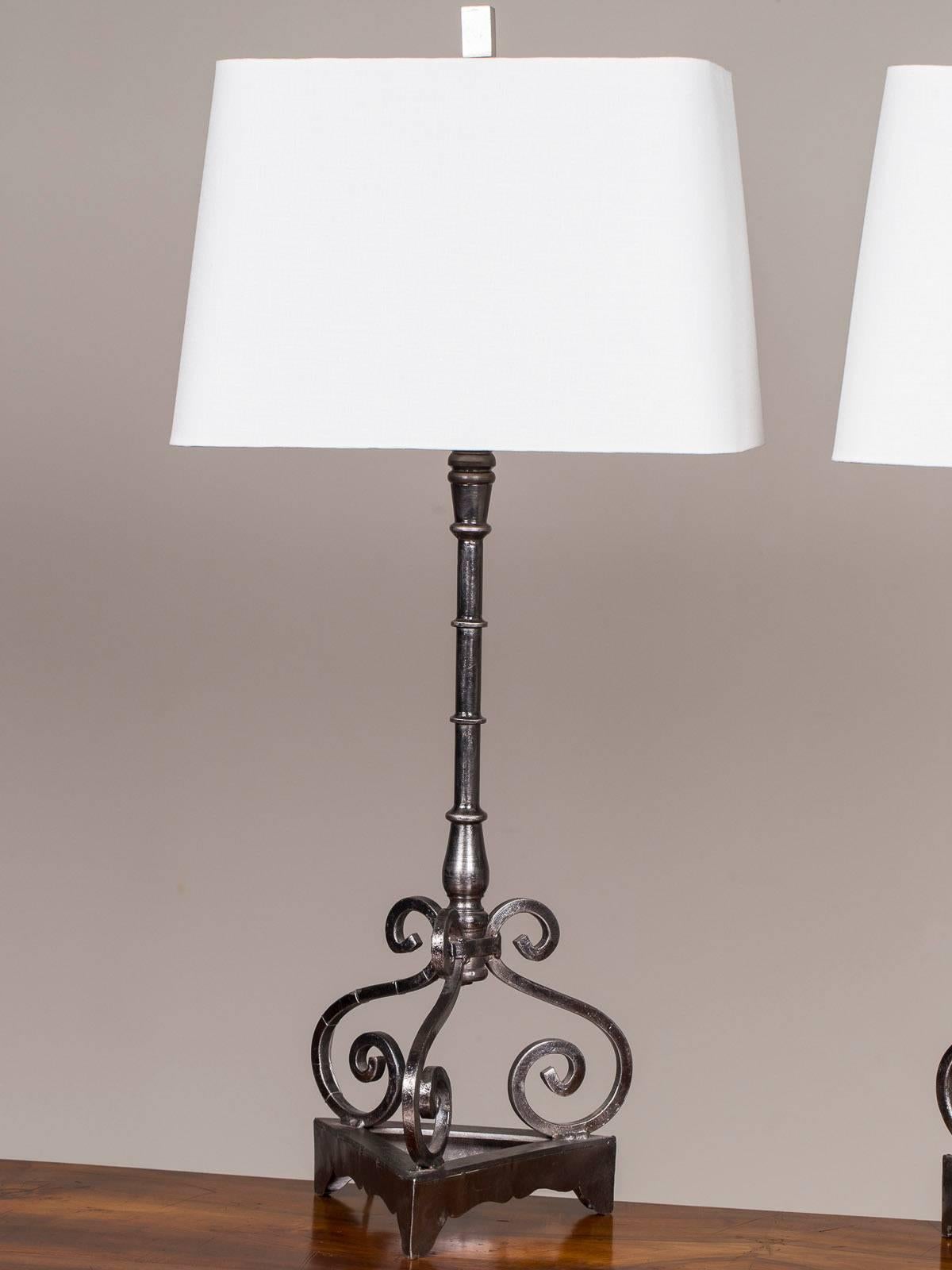 A pair of neoclassical style steel and iron modern lamps found in France. Please notice the interesting triangular base that supports three scrolled elements topped with a baluster form column. The metal possesses an intriguing finish of lights and