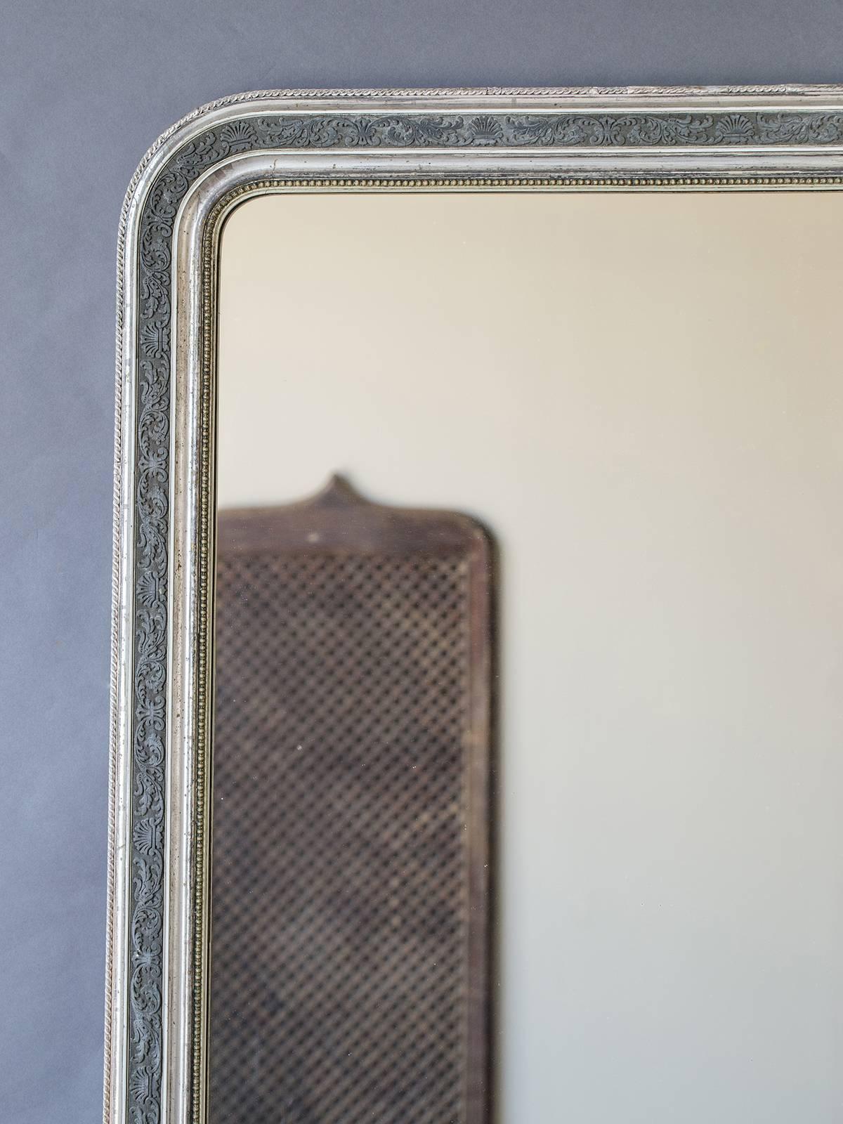 This antique French mirror has a lovely border with an impressed floral motif enhanced by the use of silver gilt. The gently rounded upper corners follow the profile of the Louis Philippe style as does the contrast between the smooth sections of the