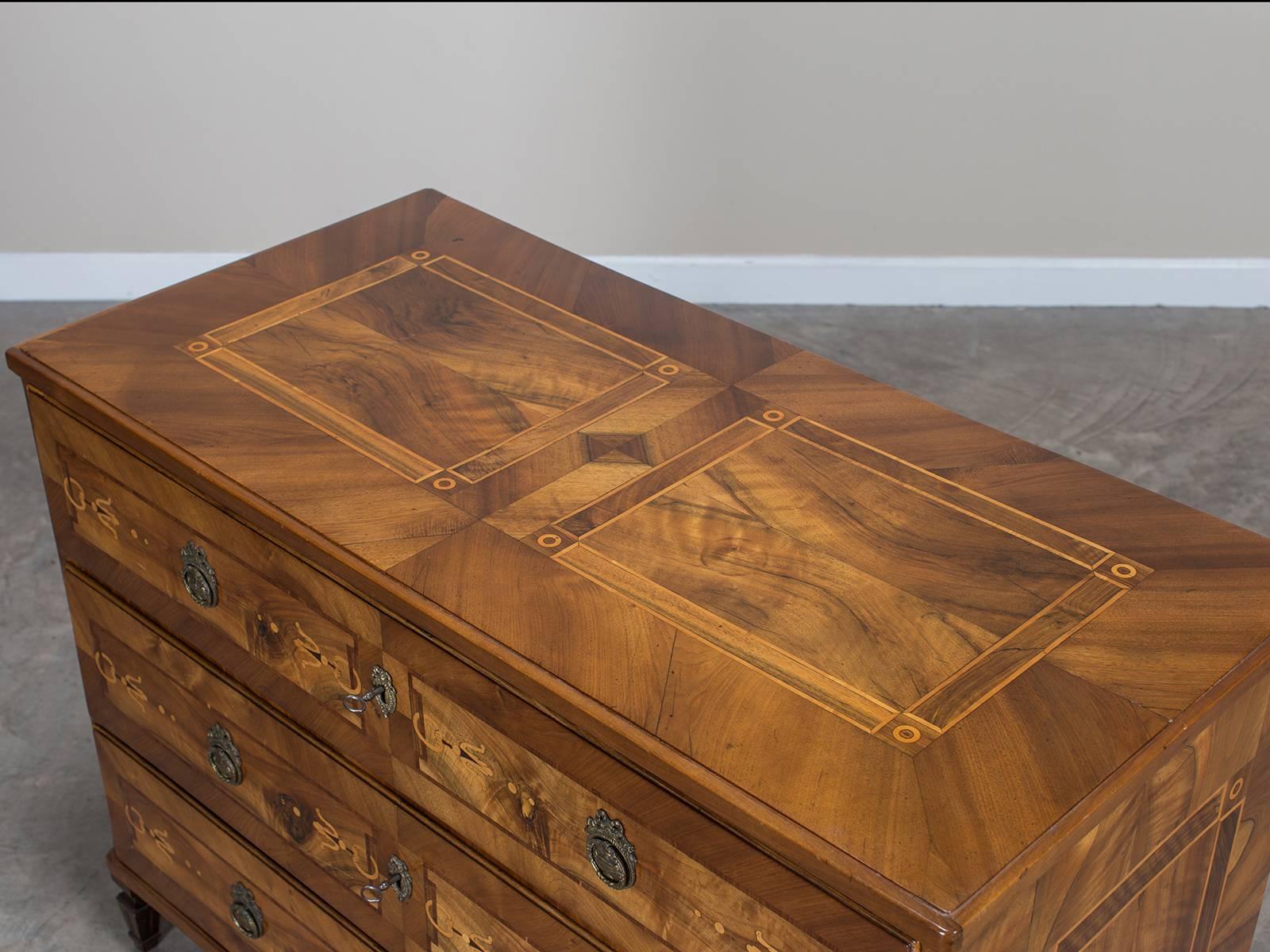The clean lines of this handsome antique German walnut chest of drawers are enhanced by the use of geometric shaped inlay in contrasting colors. The lavish use of walnut, rosewood and satinwood and the fact that the top, front and both sides are