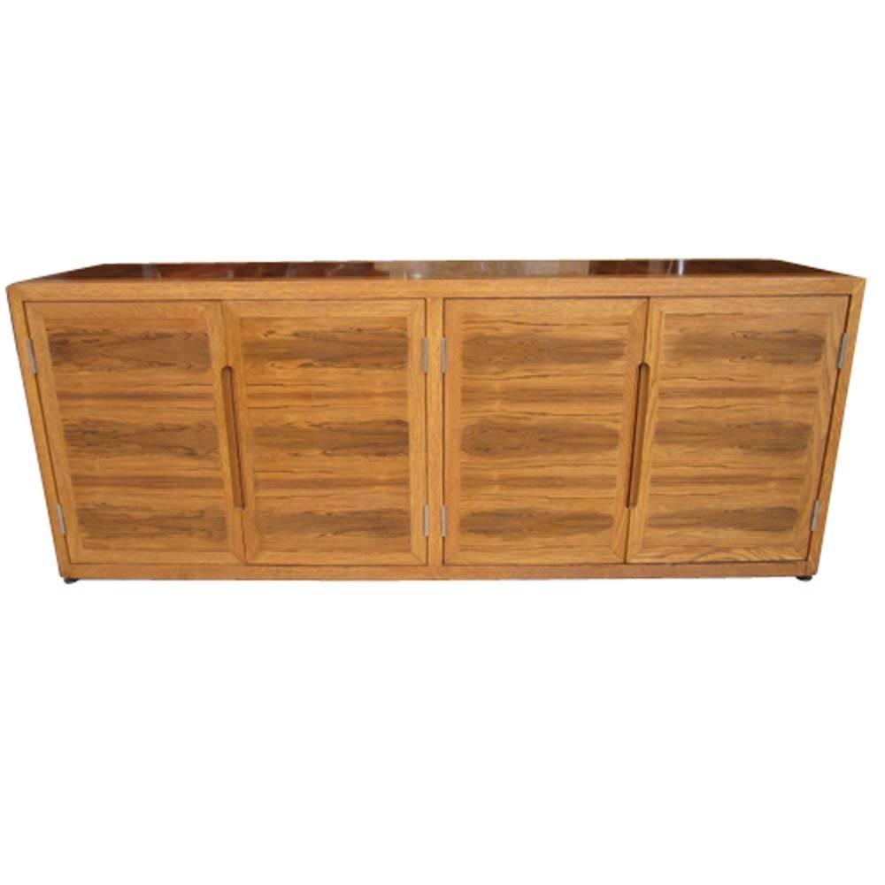 Vintage Mid-Century Dunbar credenza.

This rosewood and white oak credenza features book matched doors.
 
Oval carved door pulls.
 
Inlaid rosewood sides and top.

Credenza features four-drawer and a two shelf compartment, sits directly on