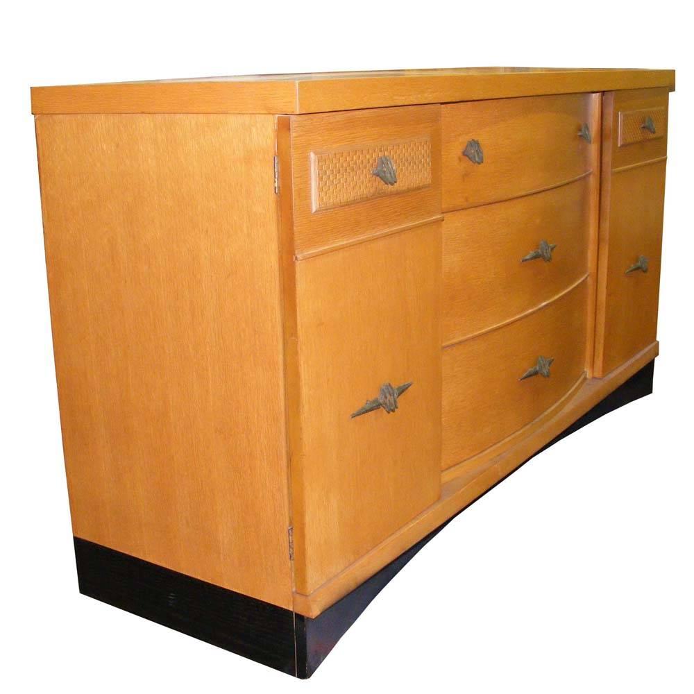 His piece boasts Art Deco design with bronze hardware, three solid wood double dovetail drawers, and two cabinets with shelving. Flatware drawer.
Base has been ebonized.