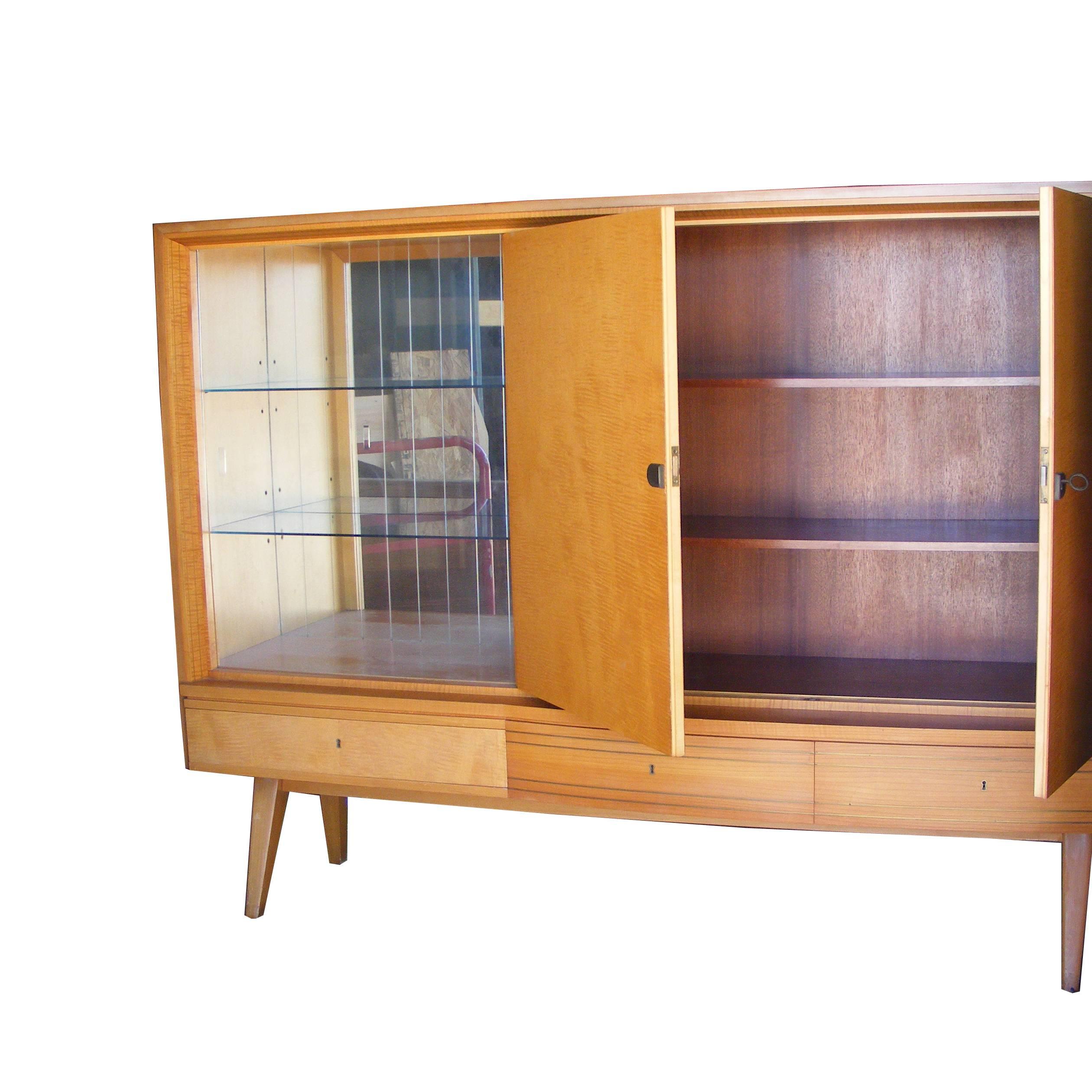 Lovely example of Mid-Century German design. Maple exterior with mahogany interiors. Can be used as bar cabinet with lots of storage. Open glass shelving with mirrored back. Two door cabinet opens to two shelves. Three locking drawers at base with