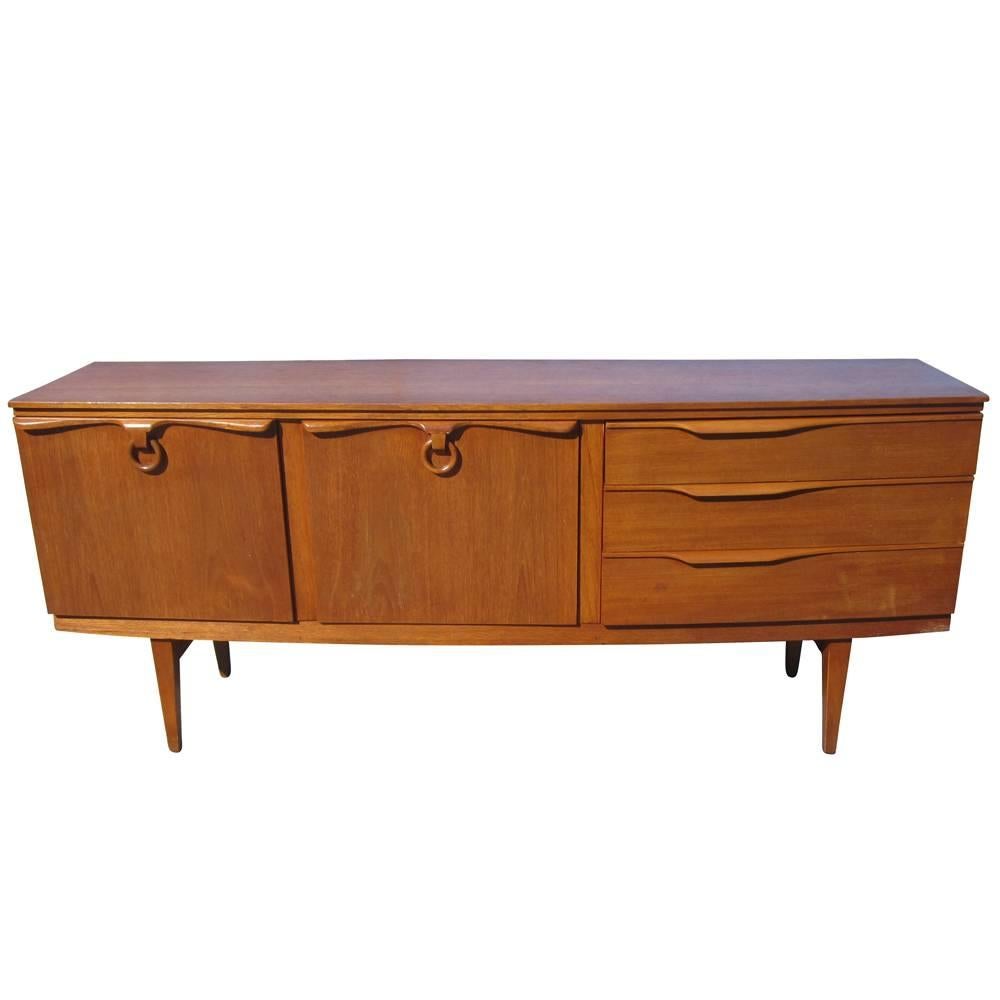 A vintage Danish style teak credenza manufactured by Beautility. This lovely sideboard features three drawers, one swinging door with two shelves, and a drop-down door. With its sculptural elements, from the wooden ring pulls, tapered legs, and