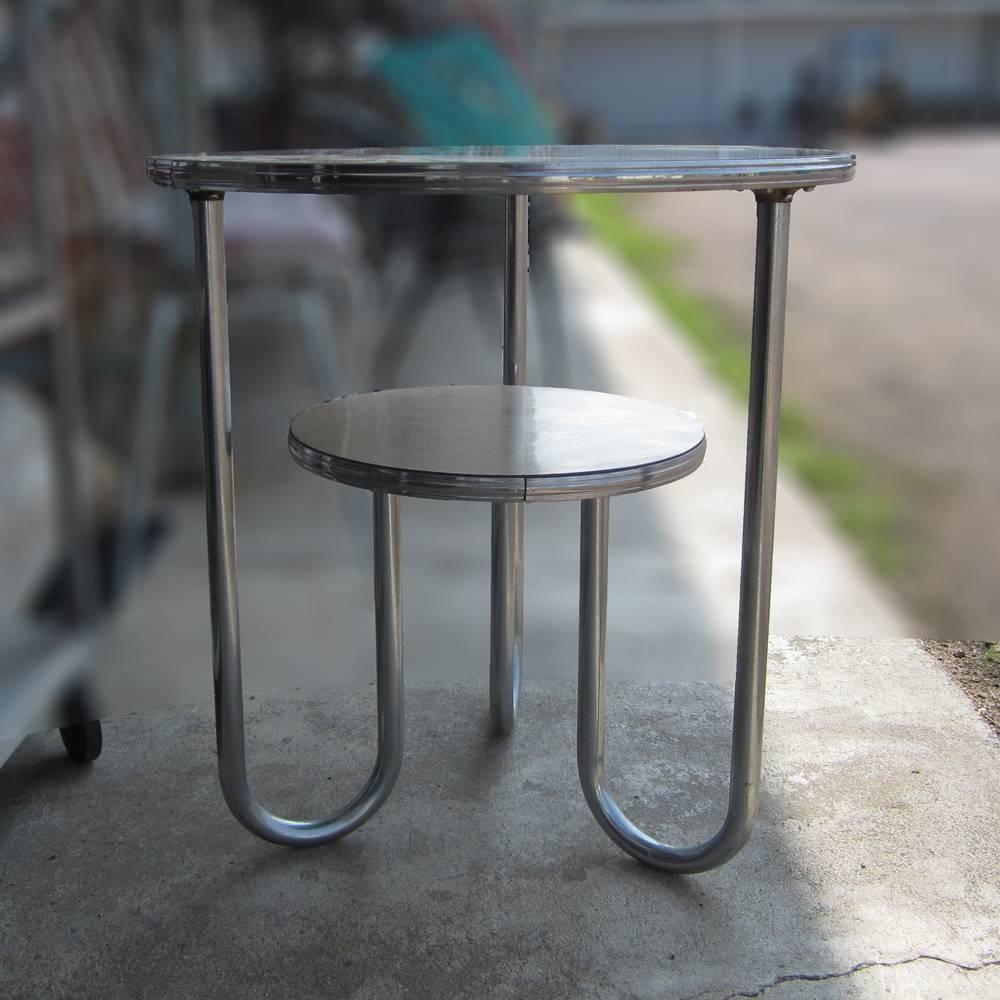 A vintage 1940's Bauhaus-Deco tiered side table designed by Wolfgang Hoffmann for Royal-Chrome
Three chrome hairpin legs curve inwards and connect to the lower level table. The tabletops are made of the original beige Formica plastic. A great
