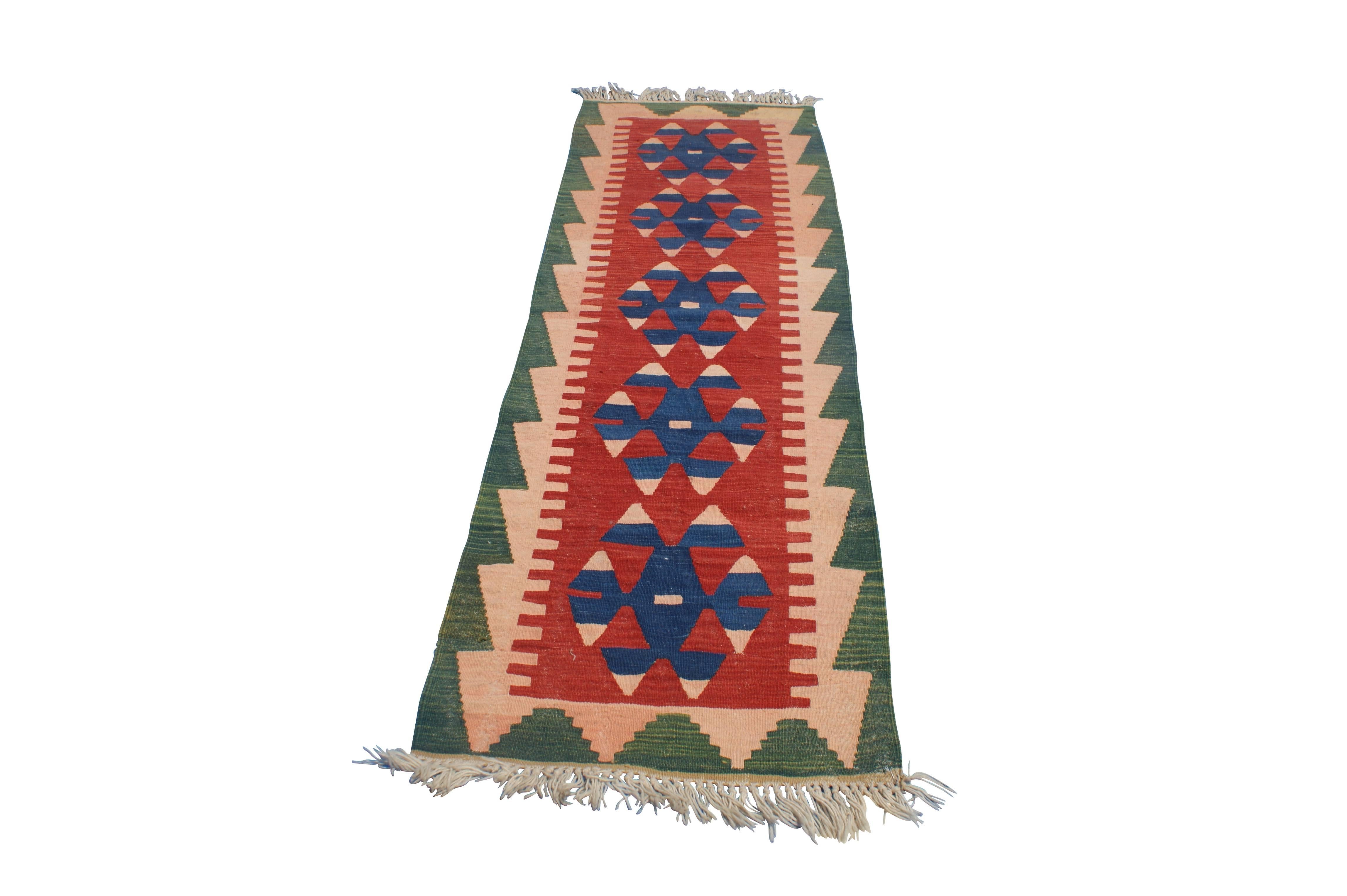 Vintage Mid-Century Turkish carpet. This geometric Kilim is made from handwoven spun wool and features vibrant red, blue, green and neutral hues. Measures: 30" x 94".