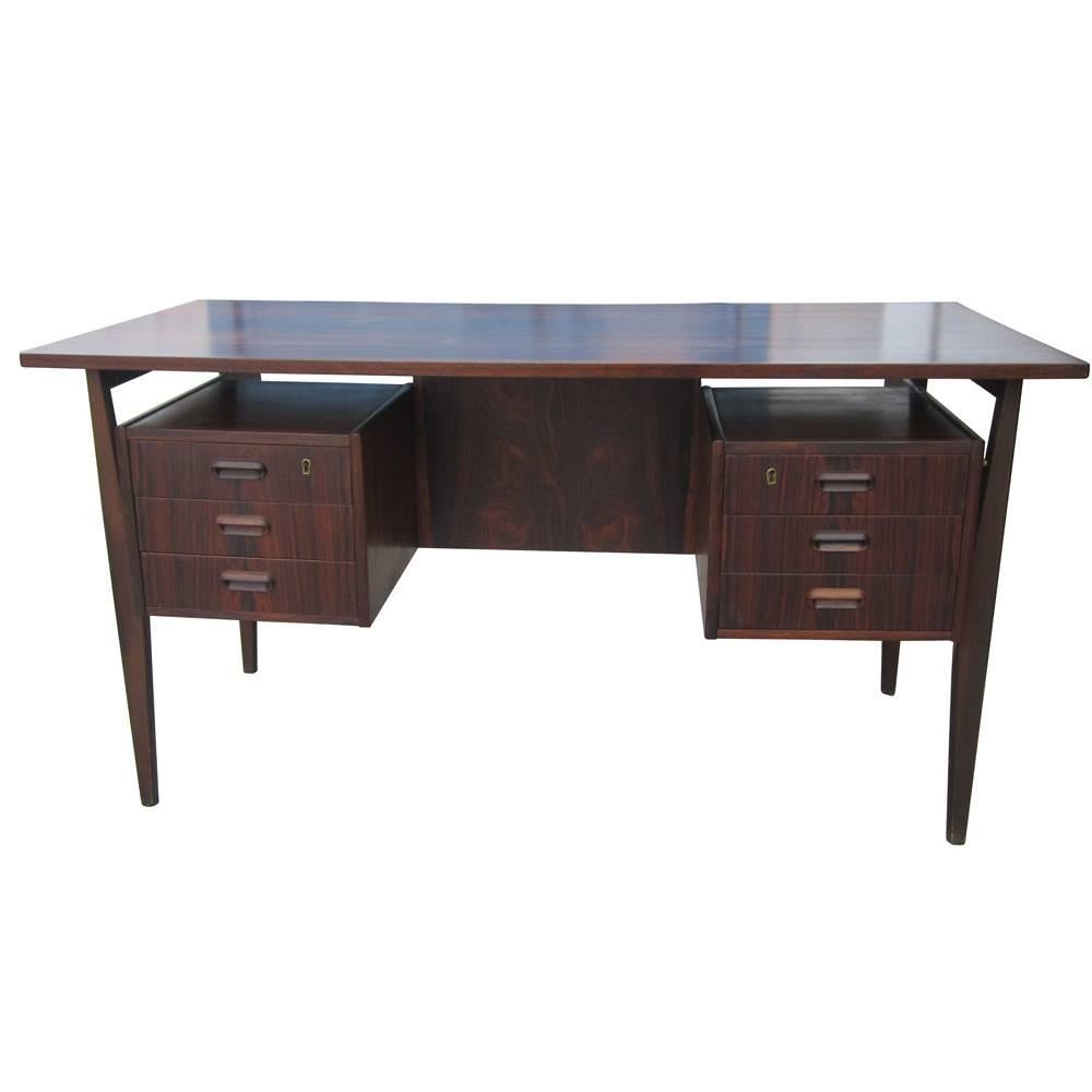 A vintage rosewood two-pedestal desk made in Denmark. Features six locking drawers with sculptural carved pulls.  Front of desk is completely finished and includes an additional storage shelf. This beautiful desk retains a natural finish that