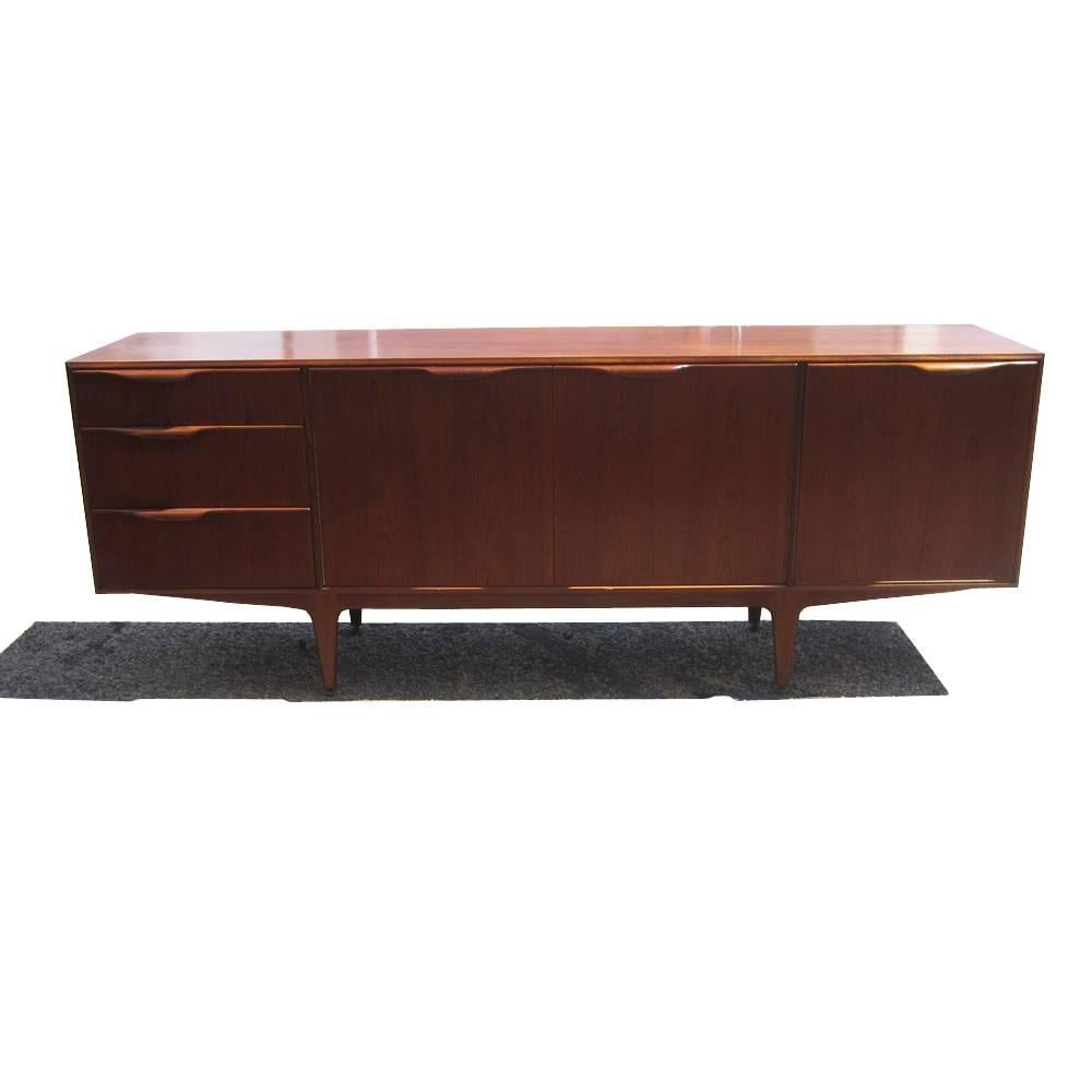 A vintage midcentury credenza from McIntosh made of teak. This spacious piece features different types of storage, including a large central cabinet with two tiers, three pull-out cutlery drawers, a drop front cabinet for bottles and a pull-out