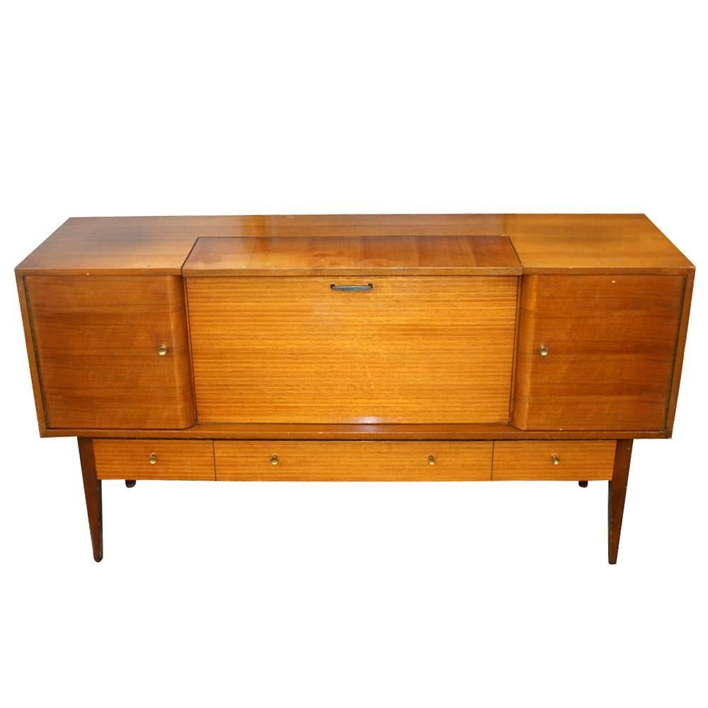Midcentury striped mahogany dry bar buffet 
Lebus of London


(Two) cabinet doors revealing shelves 
(One) pull out and (one) pull up doors for dry bar with shelf with interior light
(Four) regular drawers with antique ornamental brass pulls