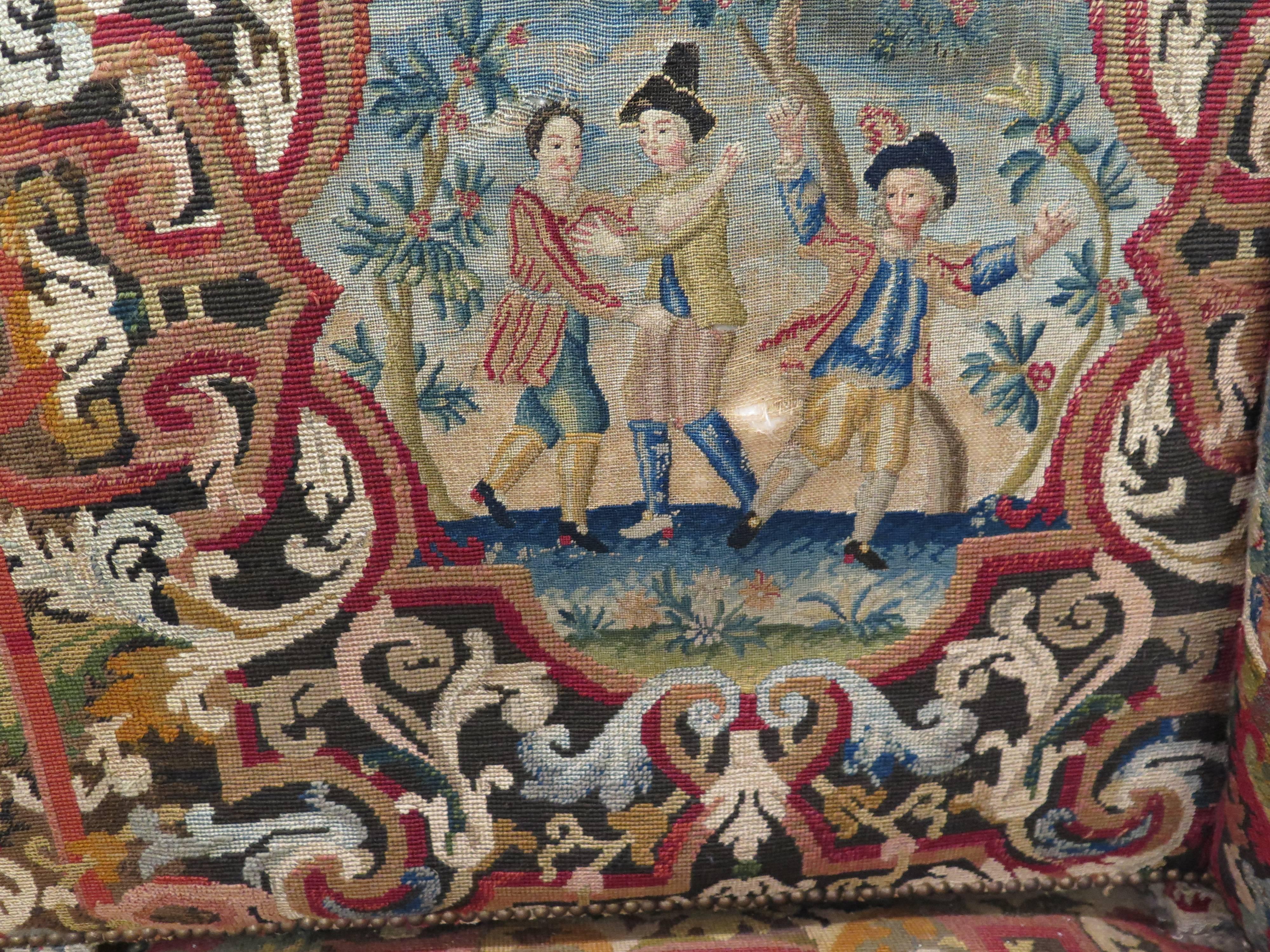 18th century French tapestry sofa with upholstered arms and nail head trim. Covered in original tapestry fabric with vivid colors featuring dancing figures, flowers and birds framed with beautiful pattern and scrolls.
 