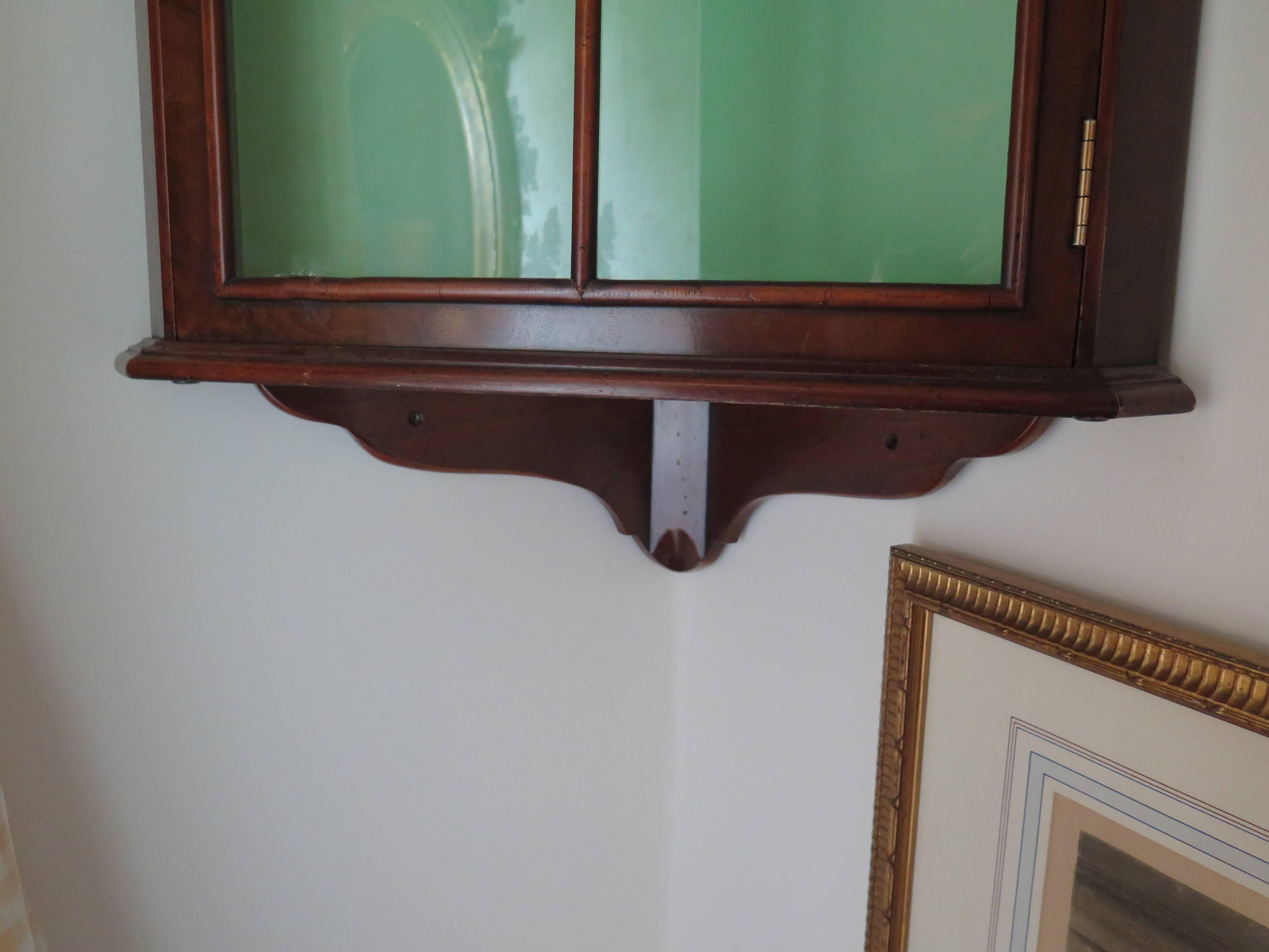 The hanging corner cabinet having a domed cornice above glazed astragal door, opening to a shleved, lined interior.