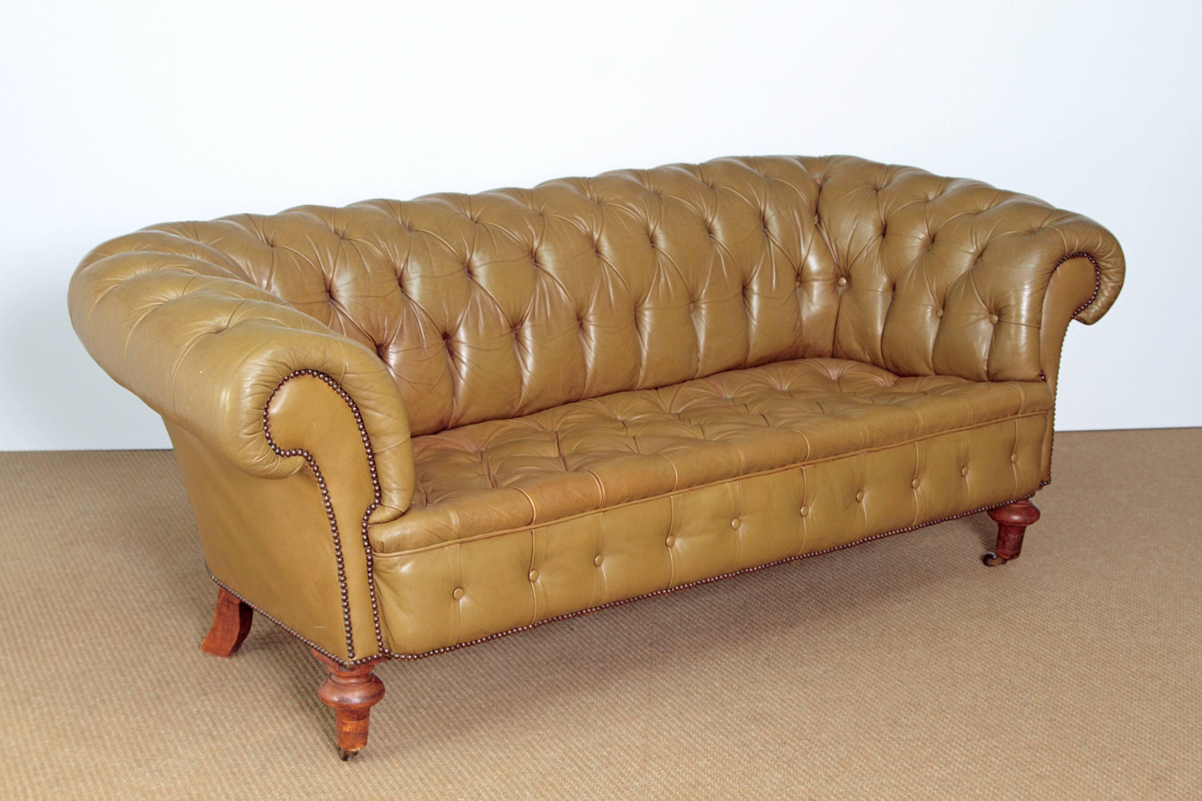 A generously proportioned 19th century English Chesterfield sofa upholstered in olive leather with nailhead trim, turned front legs with brass castors
Measures: 32inches H x 80 inches W x 36inches D.