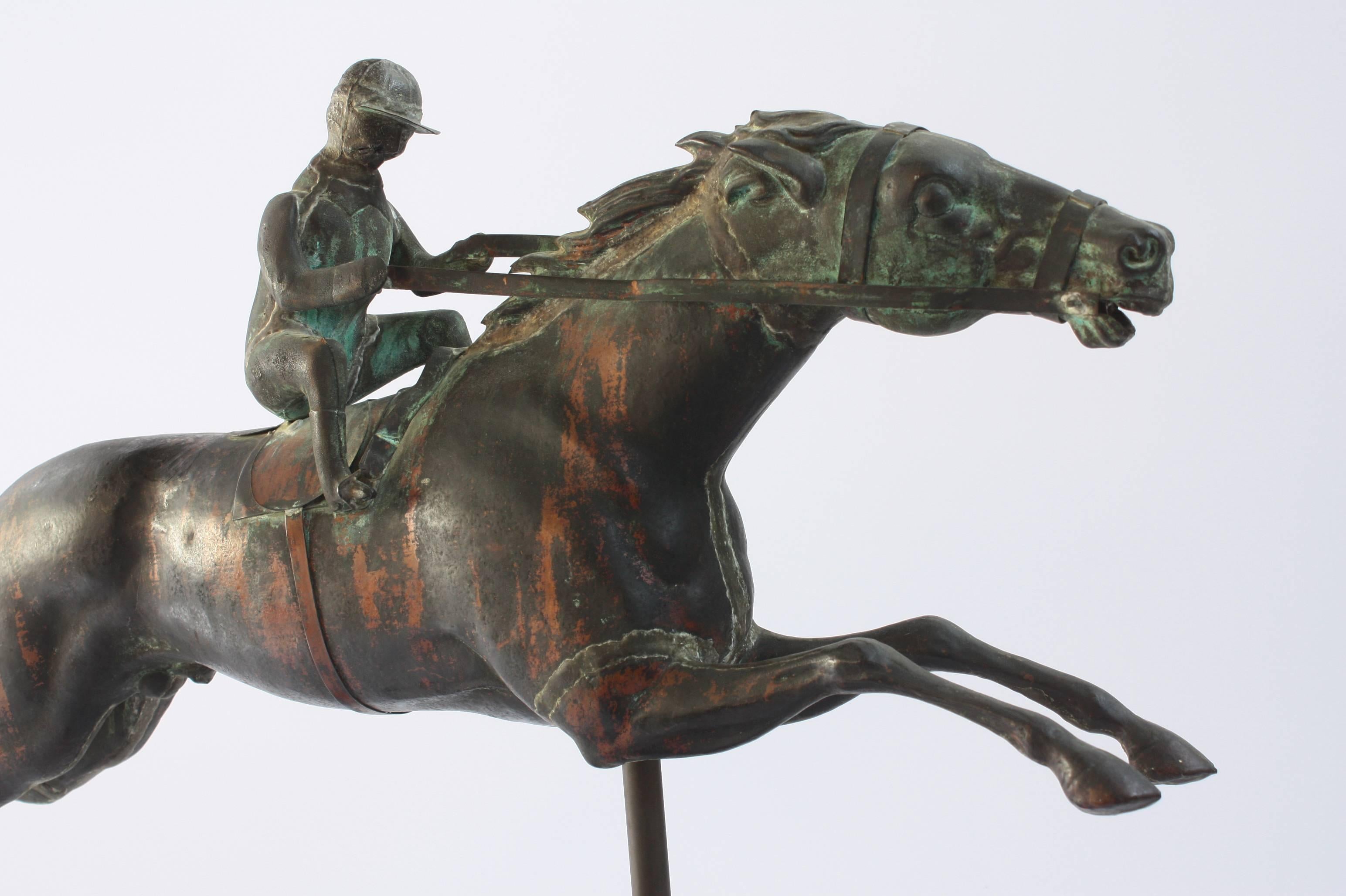 A full-bodied horse and rider or jockey weathervane with a moulded copper body and cast zinc heads, displayed on custom wooden stand or base

J. W. Fiske & Company of New York City was the most prominent American manufacturer of decorative cast