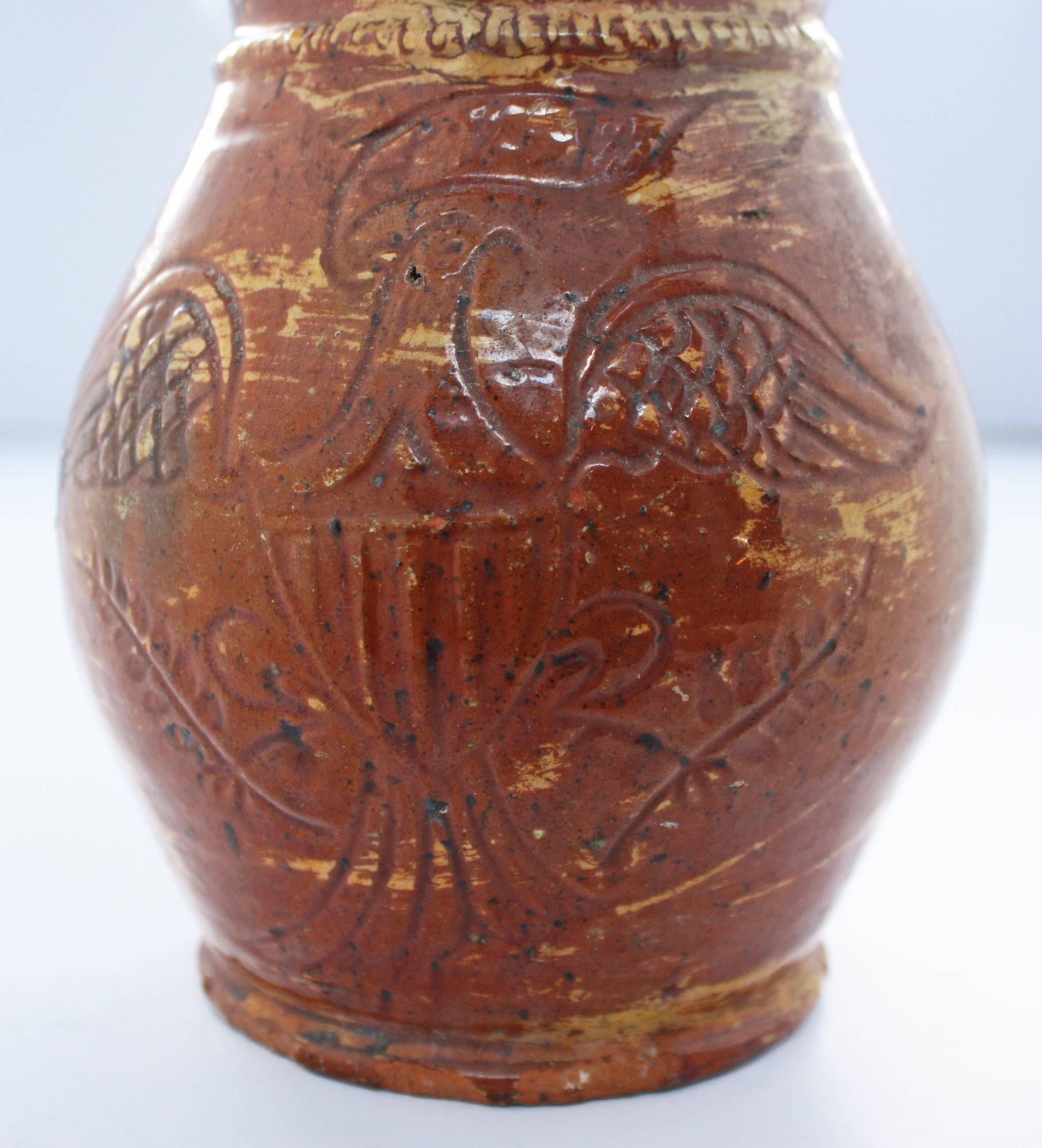 A glazed ovoid form red ware pitcher with rounded foot, ribbed handle and coggled bead below collar, decorated with a finely-incised Federal Eagle holding olive branches in its talons and a banner in its beak. Surface decorated with drips of