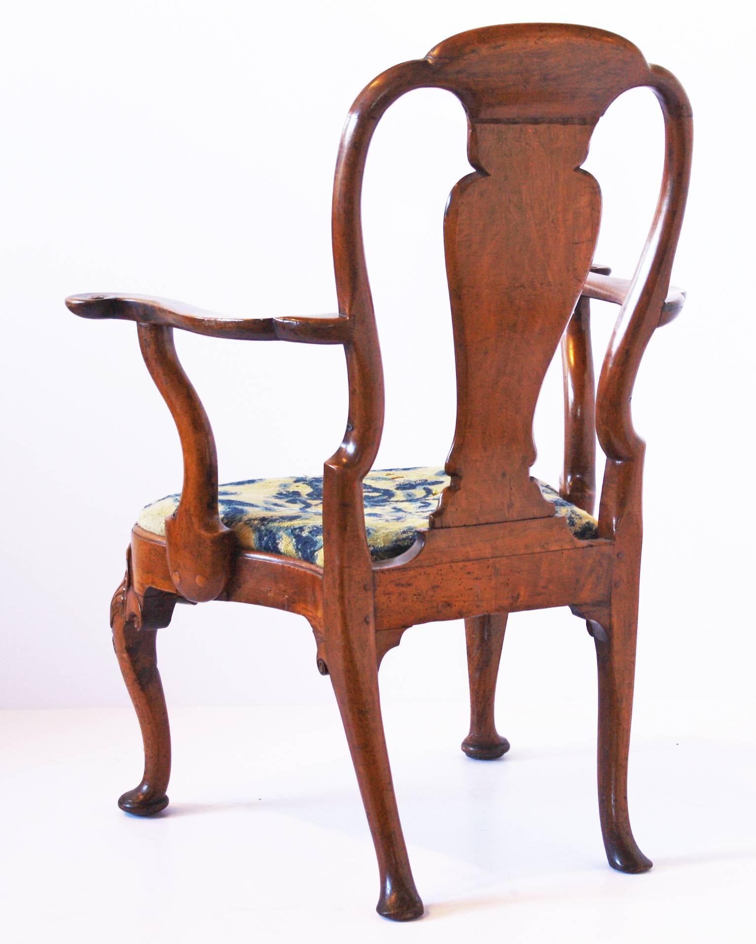 A very handsome George I walnut open armchair with scalloped curved crest rail with centered anthemion, crowning the shaped splat accented by small volute detailing and flanked by conforming stiles, the flat and outwardly oriented shaped arms