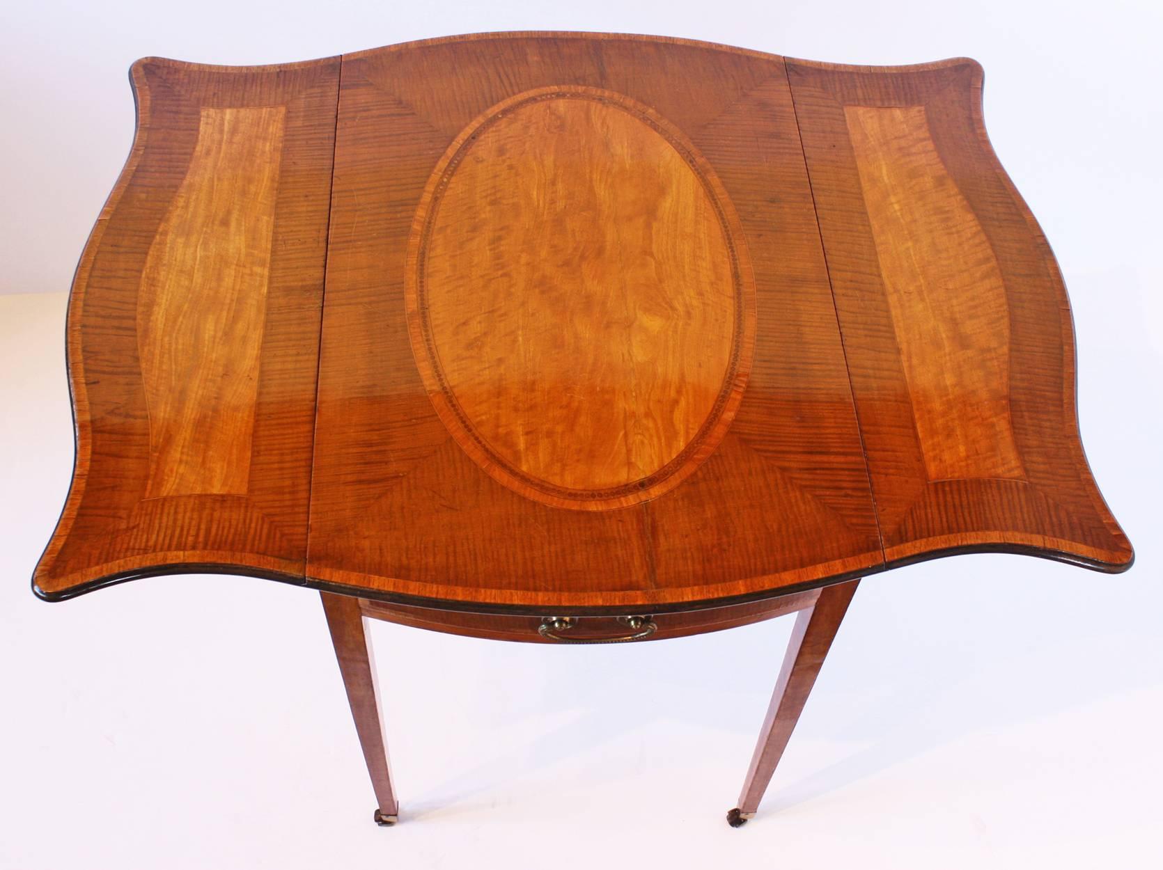 A George III sycamore and satinwood crossbanded inlaid pembroke table, rounded rectangular top centering a large oval medallion, with conformingly decorated serpentine shaped wings, above a frieze drawer, situated opposite a matching false drawer,