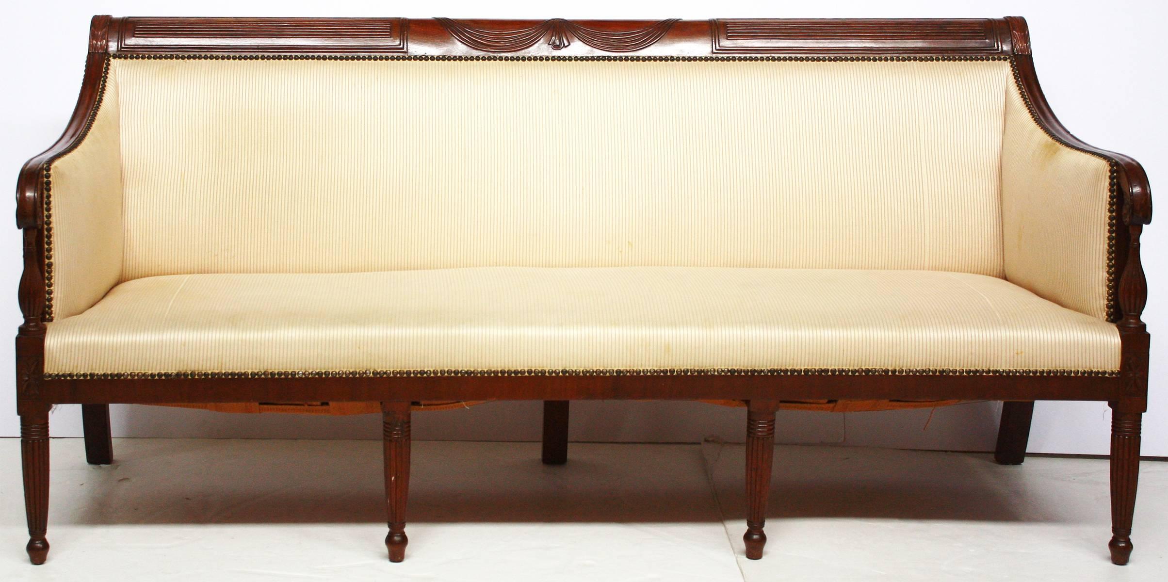 An American Federal carved seven legged mahogany sofa. Three panels of crest rail carvings: A central swag panel, with reeded panels to either side. Wheat sheaths on the corners. Curved arms with separate reeded support and legs. Upholstered in thin