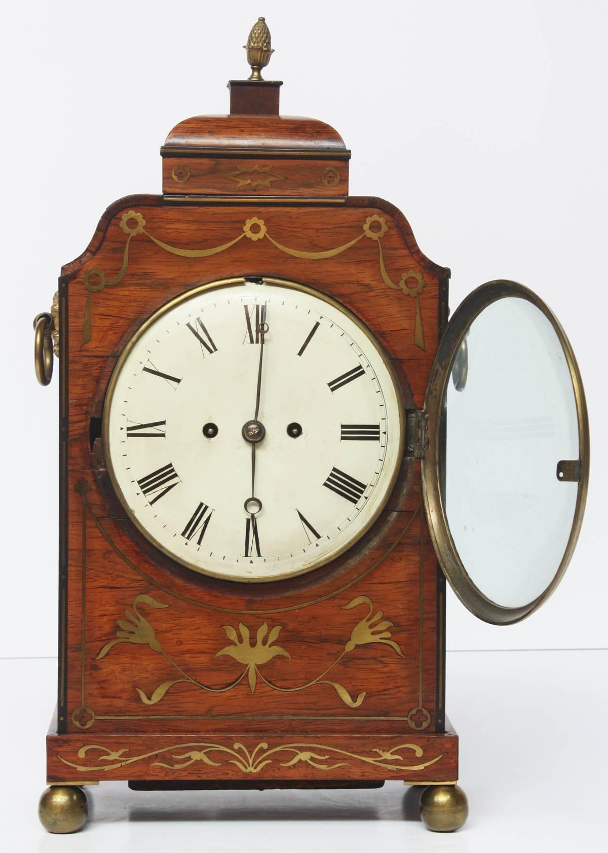 An English Regency bracket clock of rosewood with brass inlay, with a white dial. Movement is a twin fusee striking on a cast bell. The pendulum appears to be original to the movement with regulation adjustment to the top.