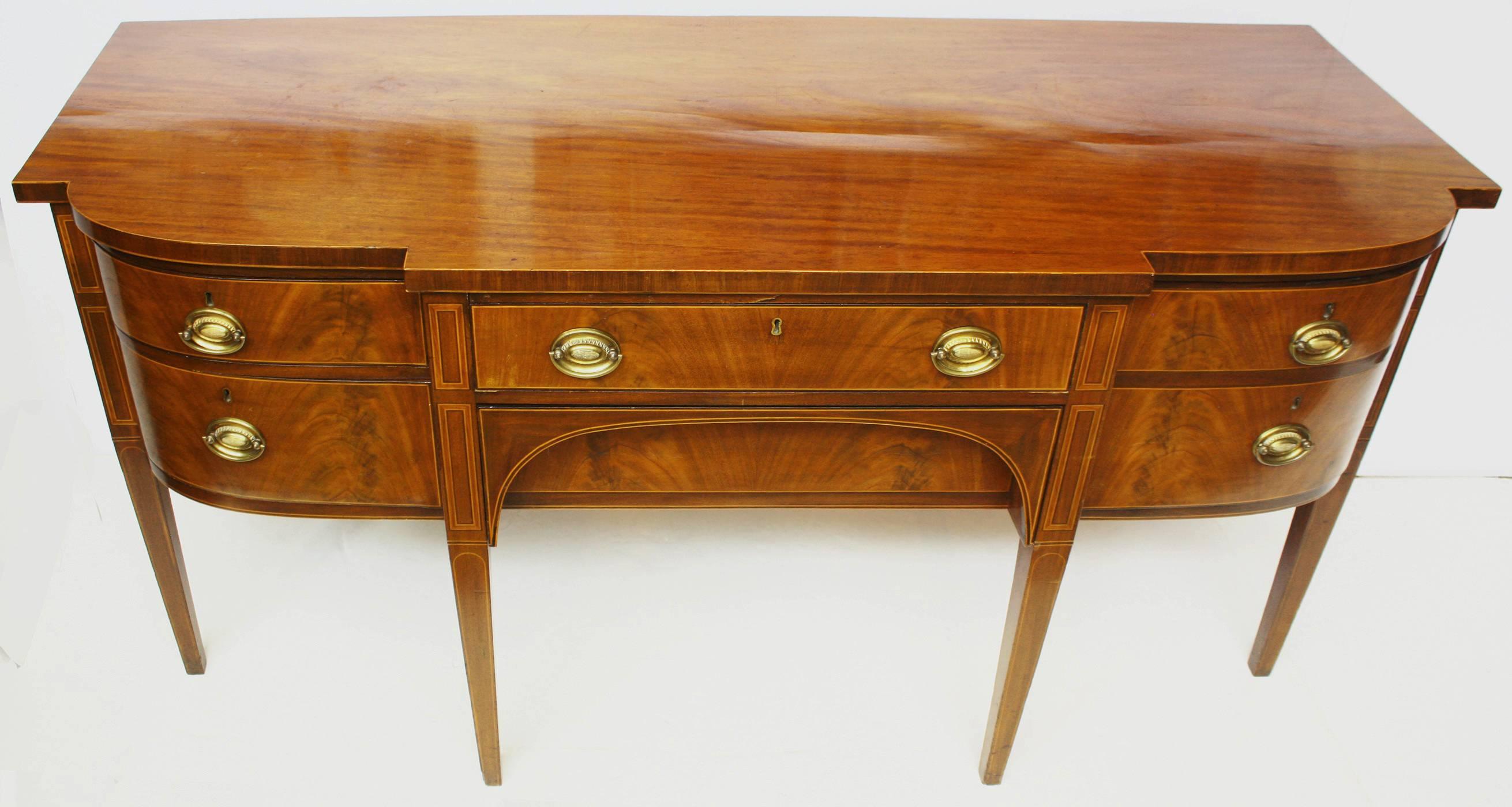 A Georgian sideboard of bookmatched crotch / flame mahogany. Wide center drawer, over an arched recessed drawer, flanked on right by a curved cellarette and a drawer and door on left, resting on tall tapered square legs. Boxwood stringing around