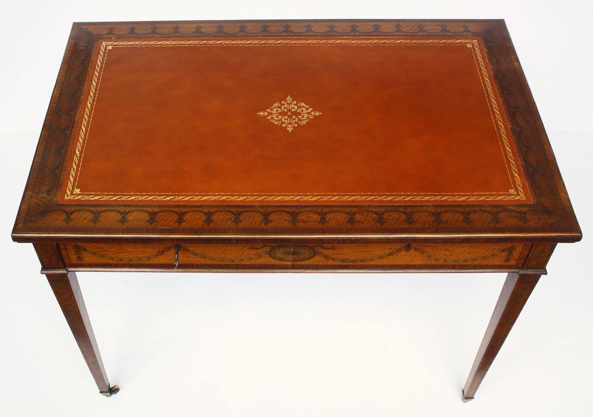 A Sheraton style, satinwood Revival writing table with a variety of inlays, scalloped border inlays with bellflower inlay top with a cross-banded edge. Bellflower inlay swags and bellflower chains across the long single drawer, apron and down each