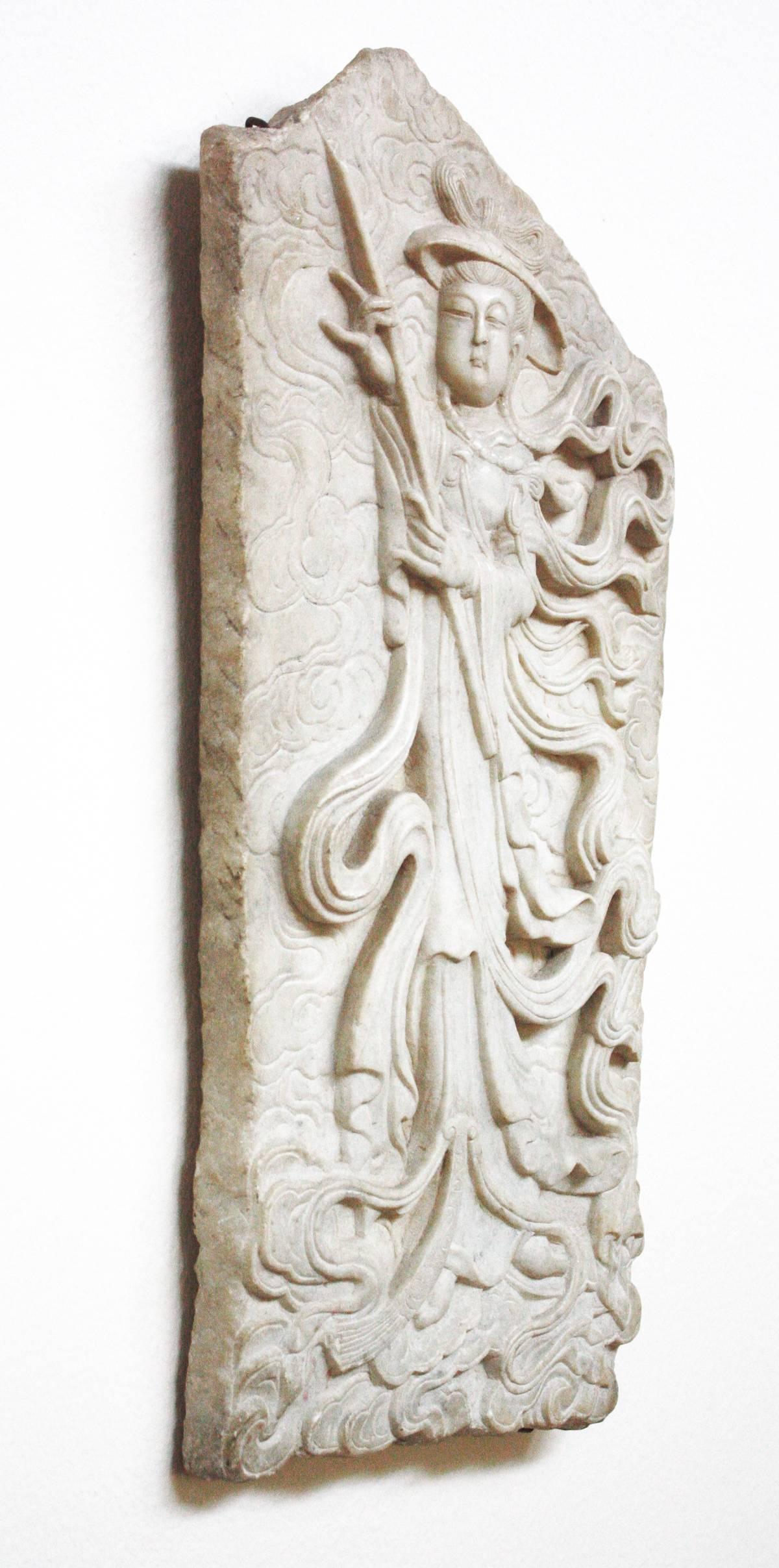 An antique Japanese marble wall carving in bas-relief of a male figure with swirling ribbons from his coat and carrying a long wand.