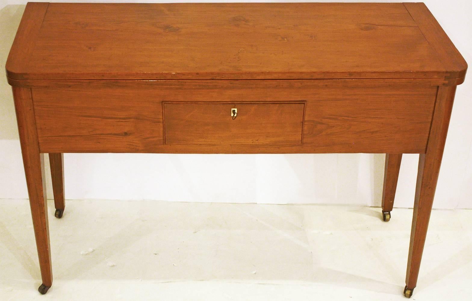 A small pine sideboard / table with flip top that swivels (so that one might sit comfortably under it on either end), single small drawer with ivory-like keyhole escucheon (with key), four (4) tapered pencil legs with brass castors, handmade,