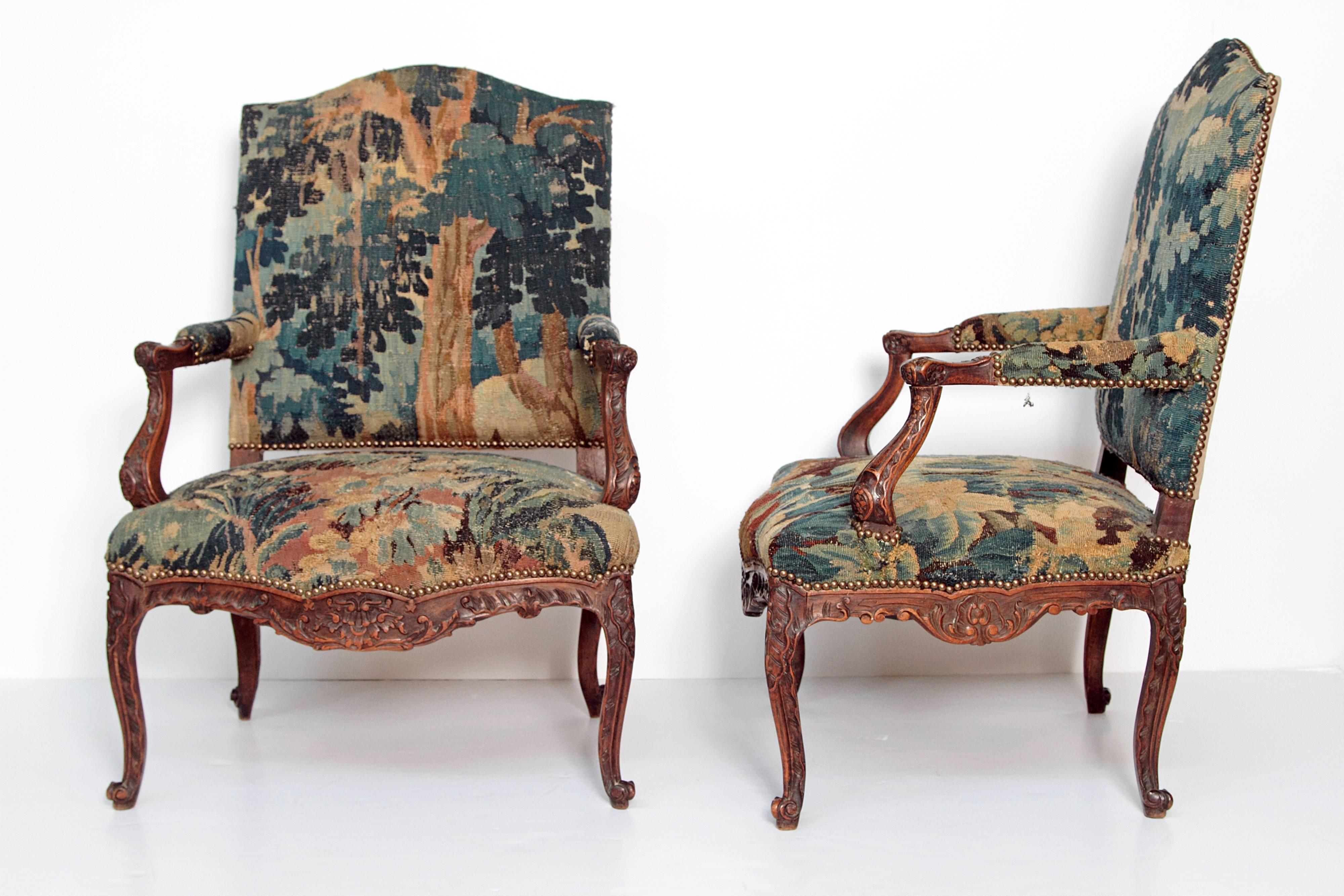 A generously proportioned pair of mid-18th century, Louis XV, hand-carved walnut armchairs with 18th century tapestry upholstery, shades of green with blue, brown, gold, and tan (leafy forest or foliate), nail head trim, chair back is upholstered in