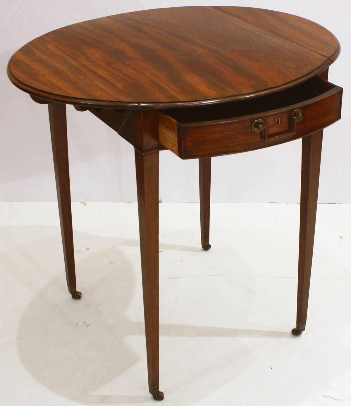A Georgian pembroke table of figured mahogany with one bowed drawer with cockbeading, small drop leaves (oval when leaves are up), and tapered pencil legs with small castors.

Measures: 19